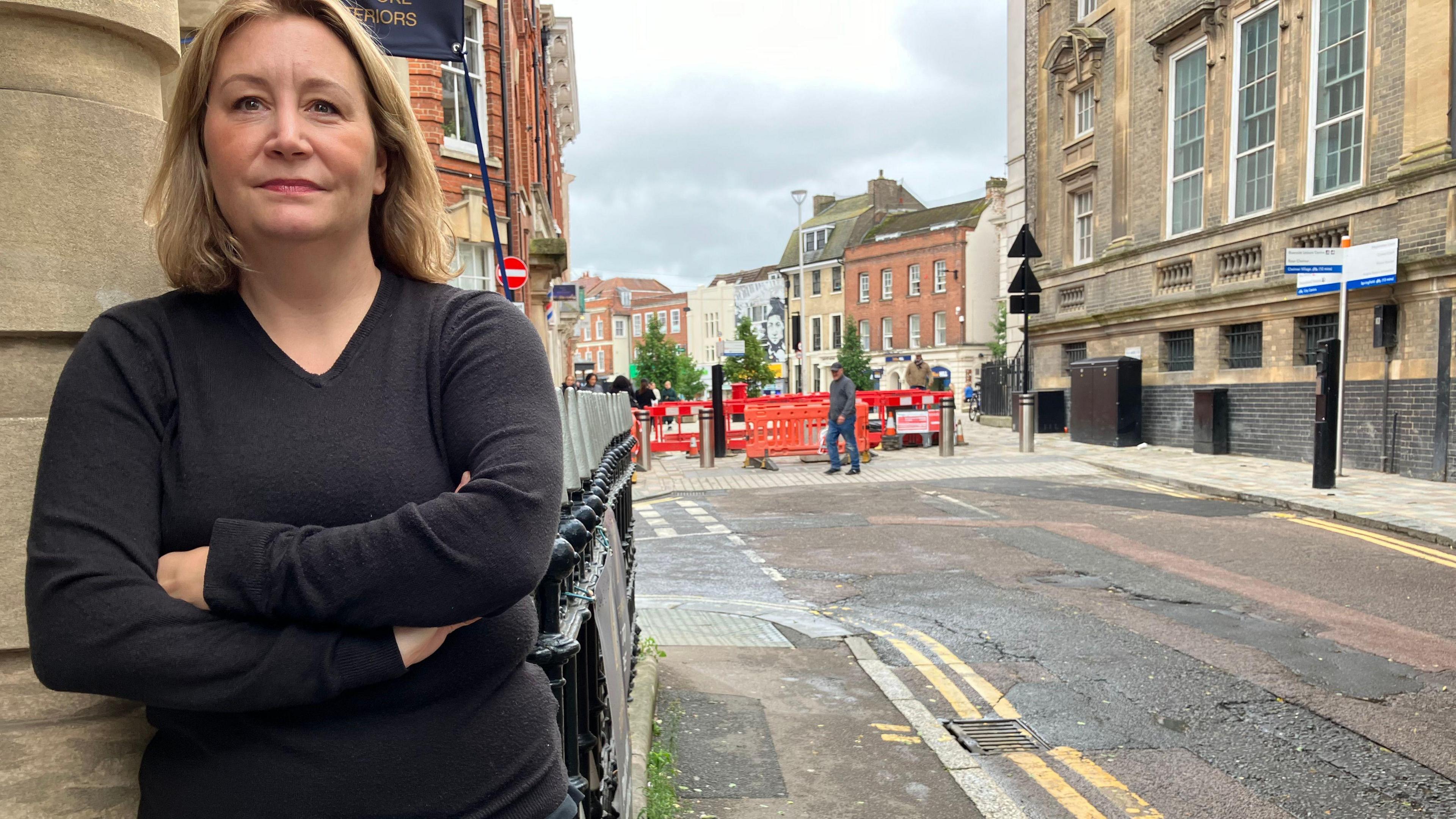 A woman with her arms folded, with her business and the roadworks behind her