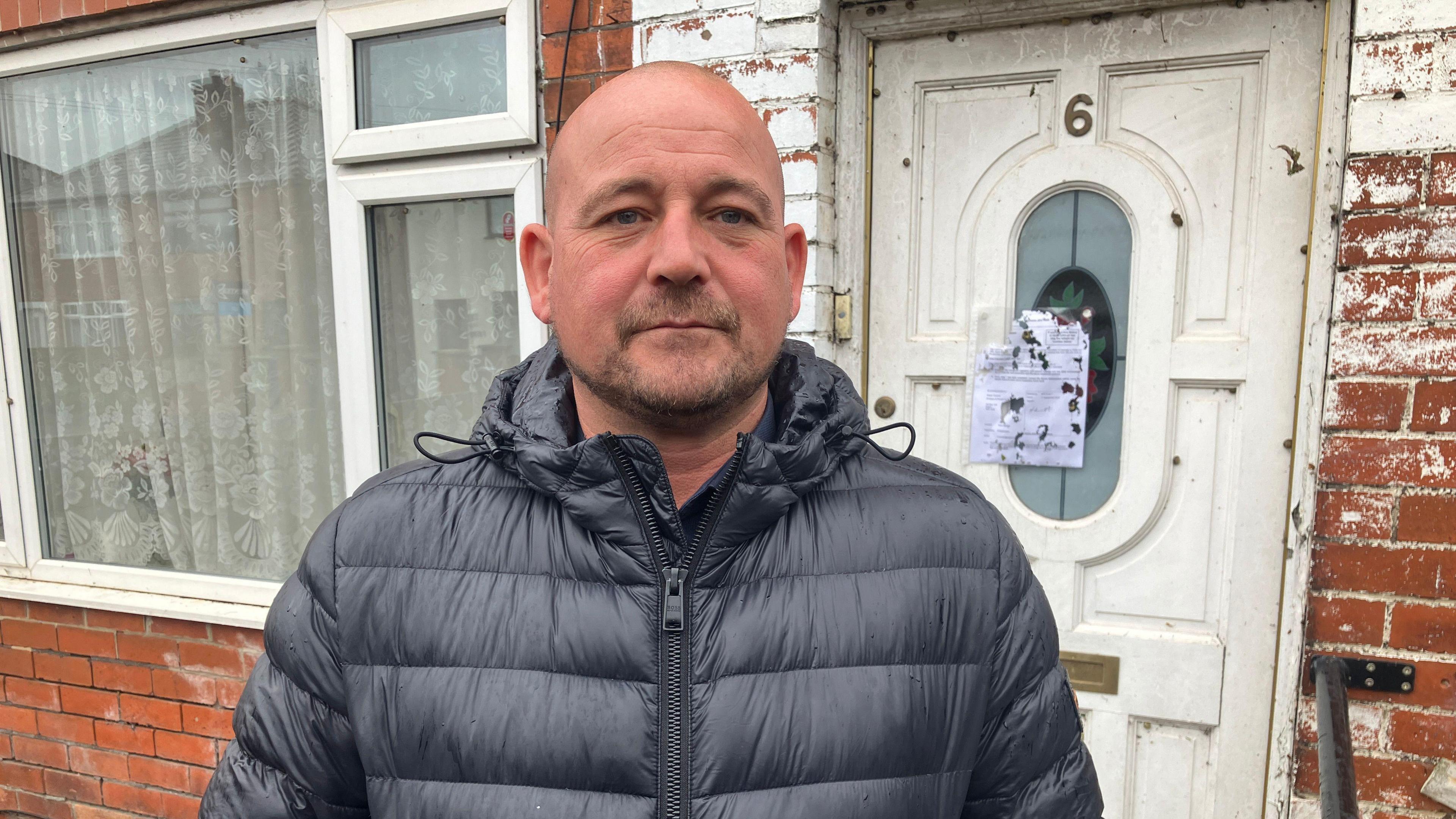 Neil Tonge standing in from of an empty house with a Prevention of Damage by Pests Act notice eaten by snails