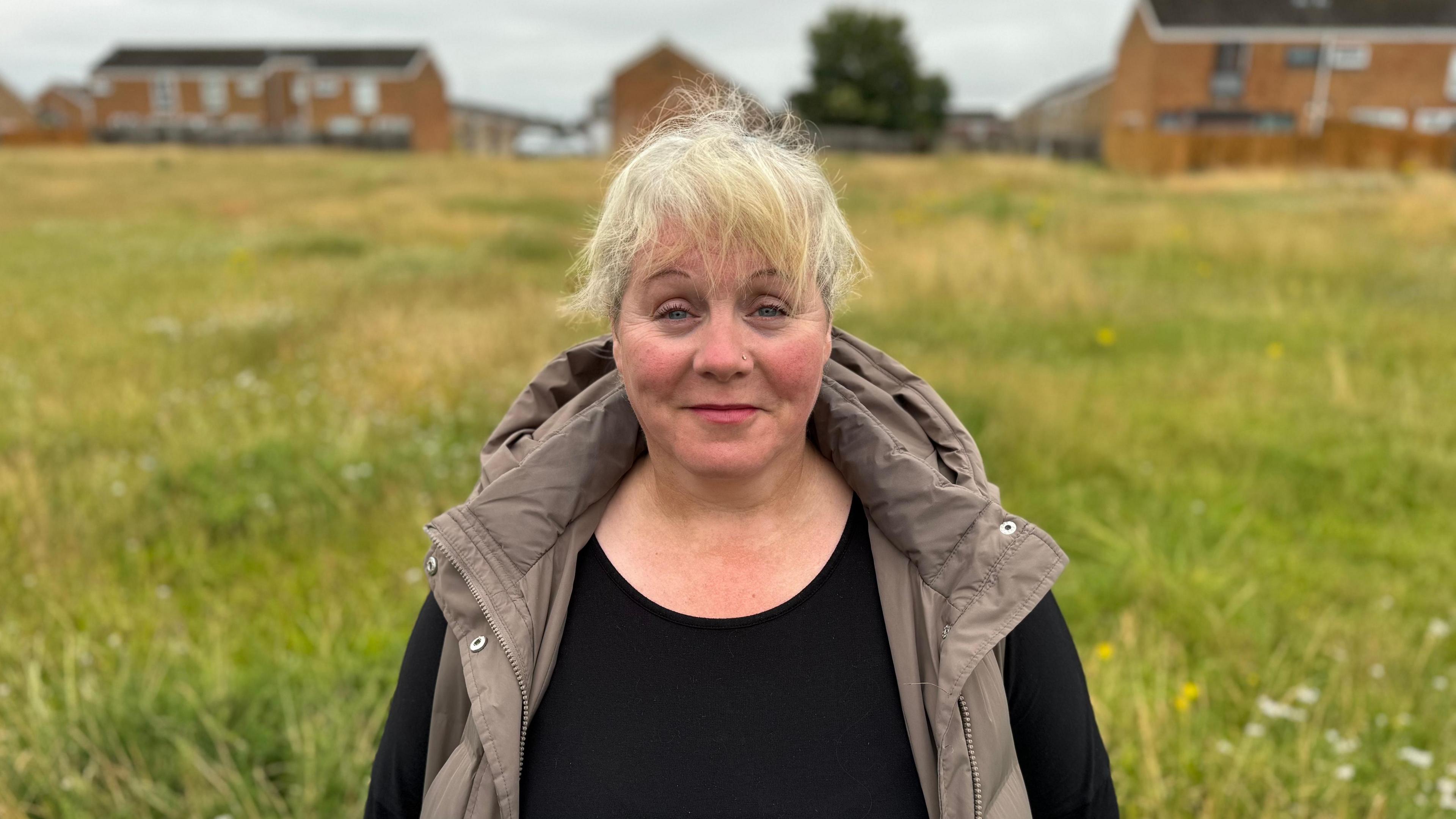 Jane Seaney smiling in a field. She is wearing a black long-sleeved top with a taupe gilet over it