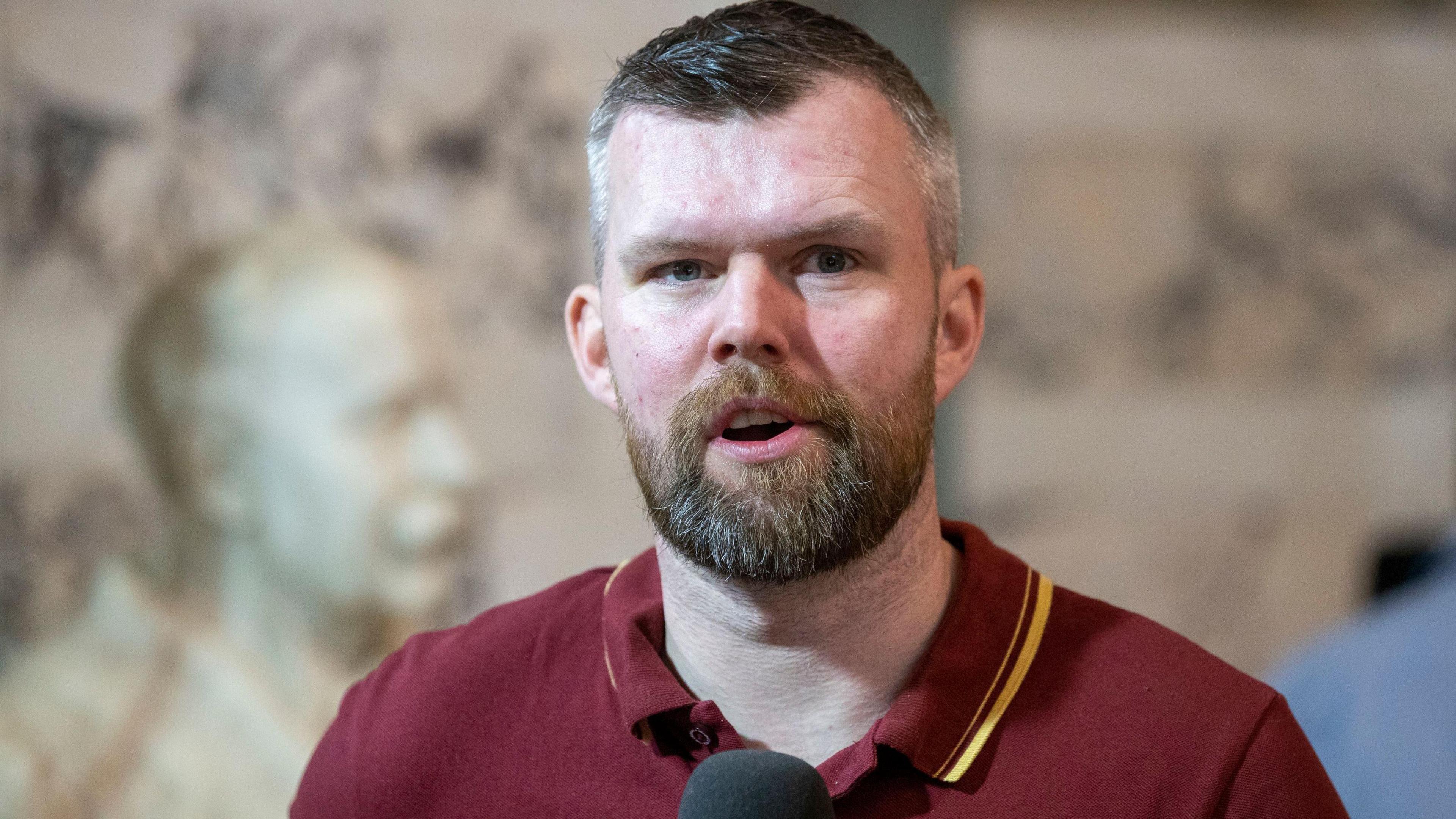 Gerry Carroll, he has dark hair and a beard and a maroon polo.