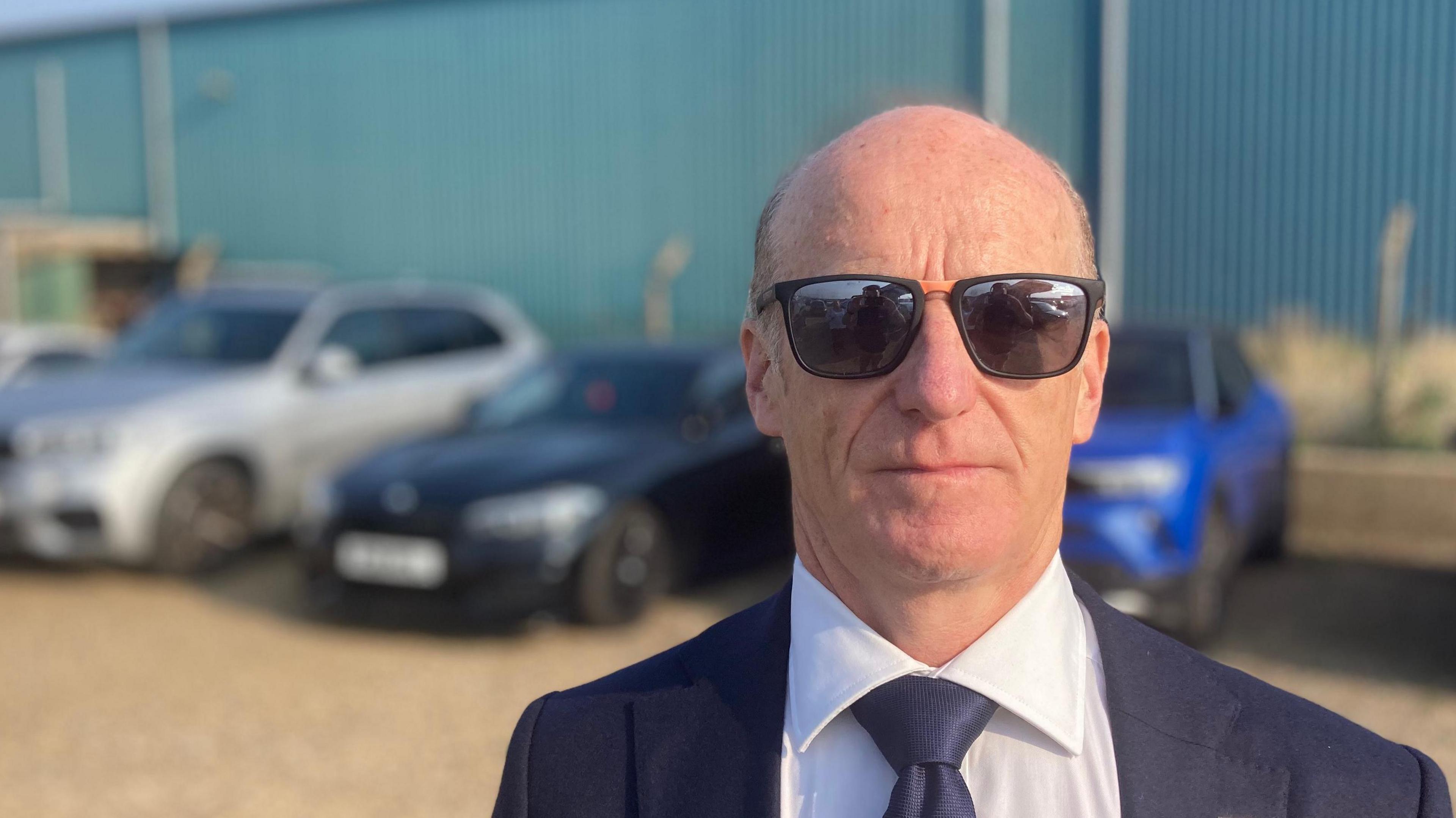 Kevin Keable of the East of England Energy Group is pictured wearing dark sunglasses while wearing a navy suit, white shirt and navy tie. 