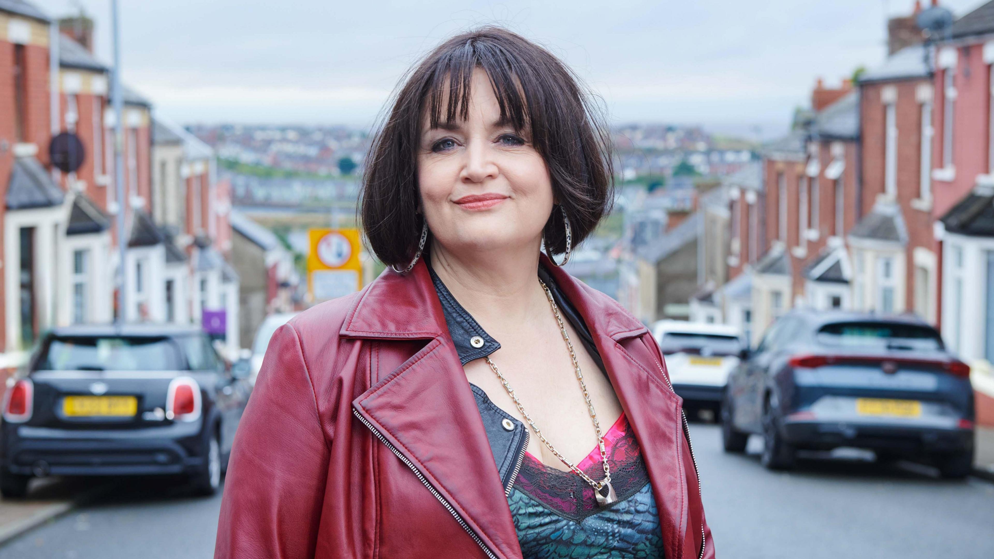 Ruth Jones as Nessa, pictured smiling while wearing a dark red leather jacket on the streets of Barry