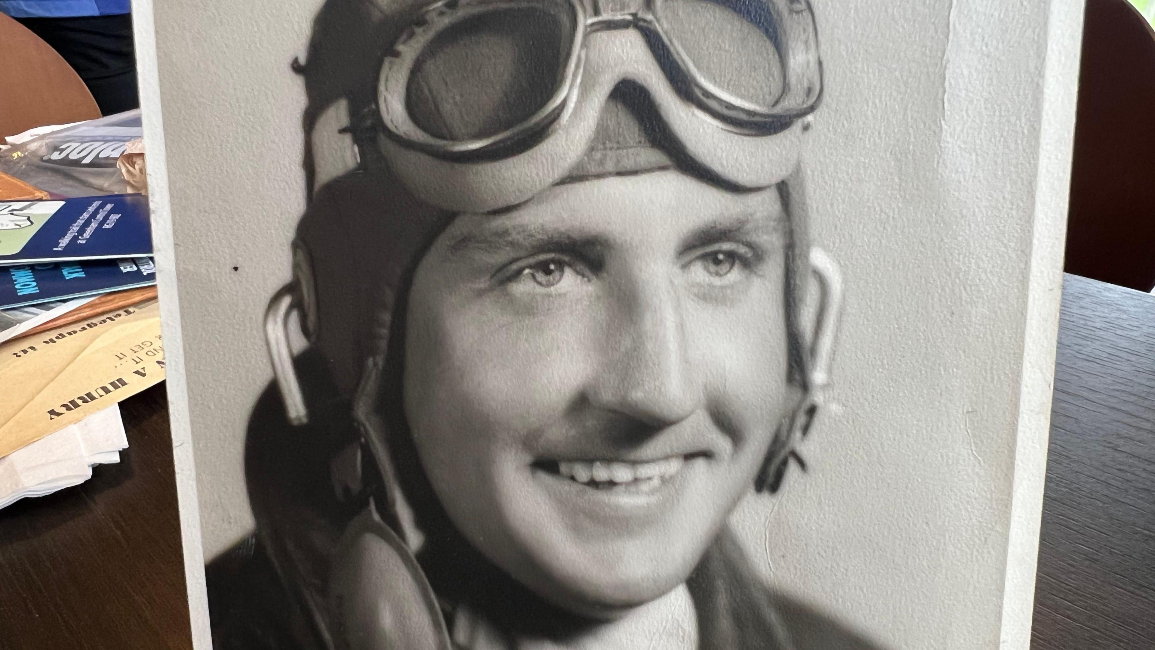 A picture of a black and white photo of a young man wearing pilot goggles on his head.