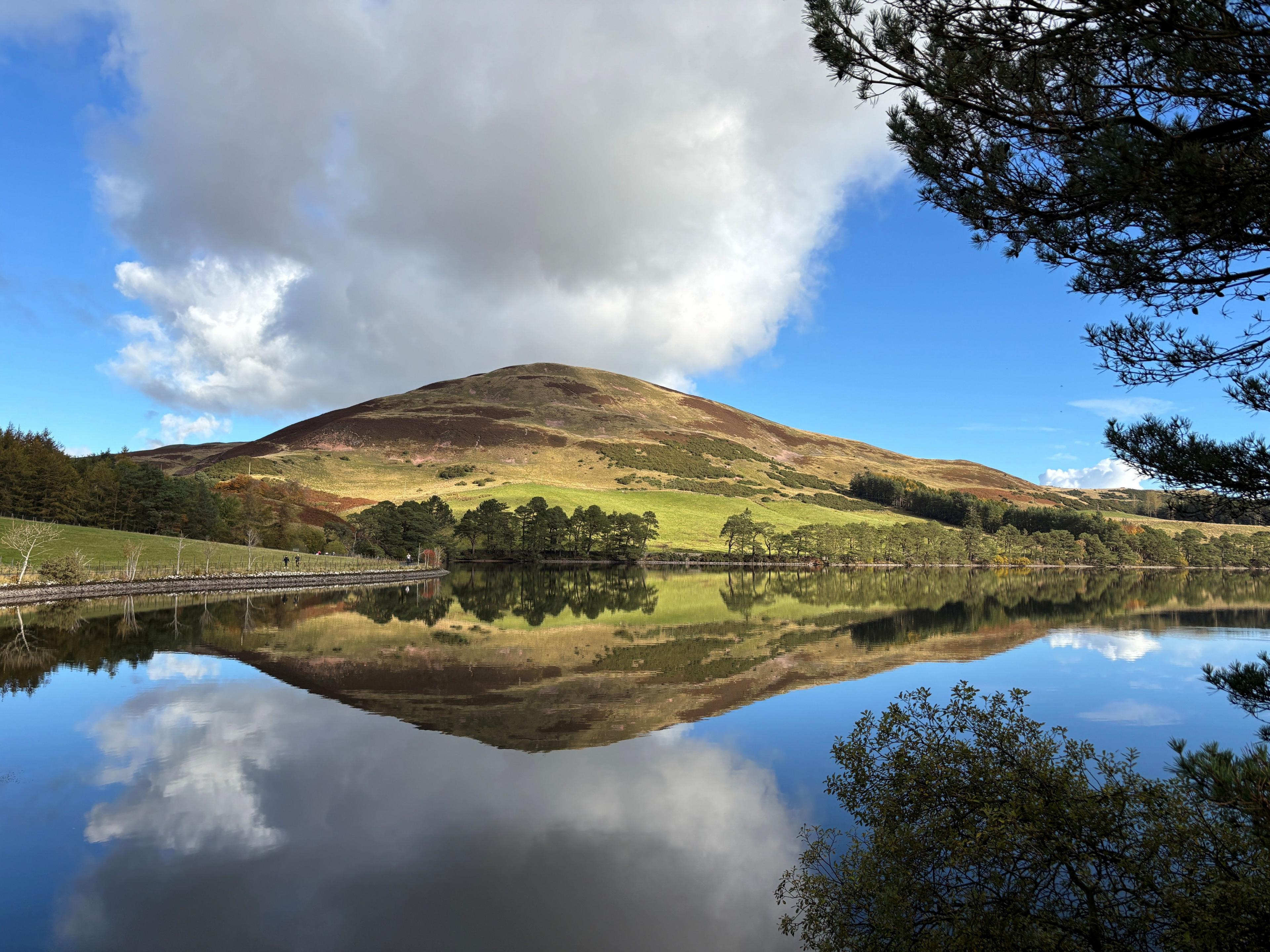 A reservoir with the sun shining down on the water and the grassy hills beyond it