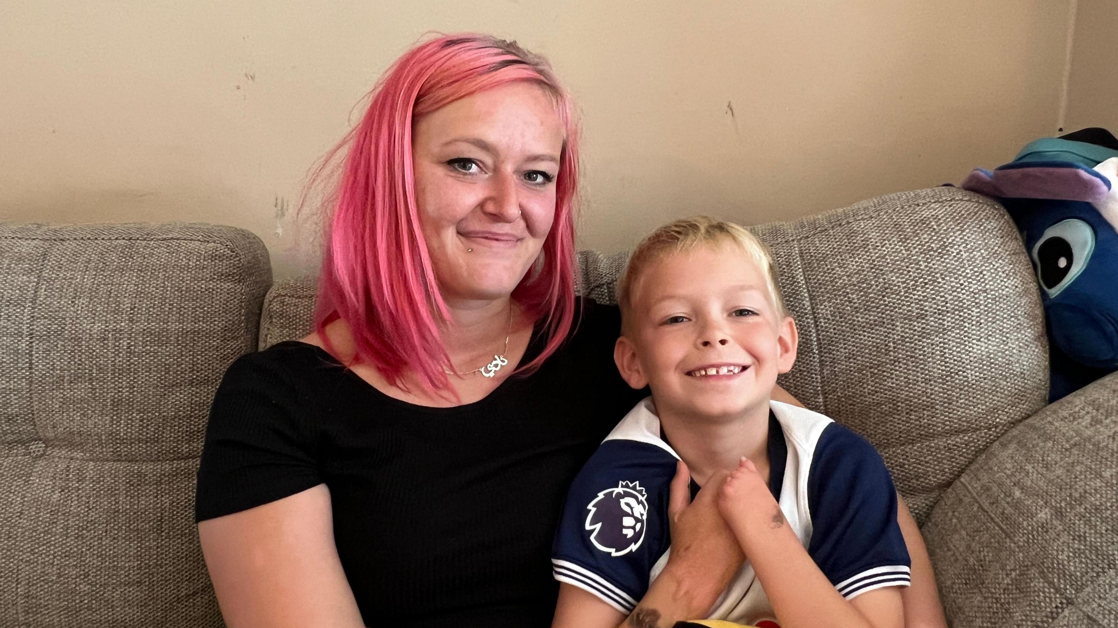 Brodie and his mum Naomi sitting on a sofa smiling into the camera