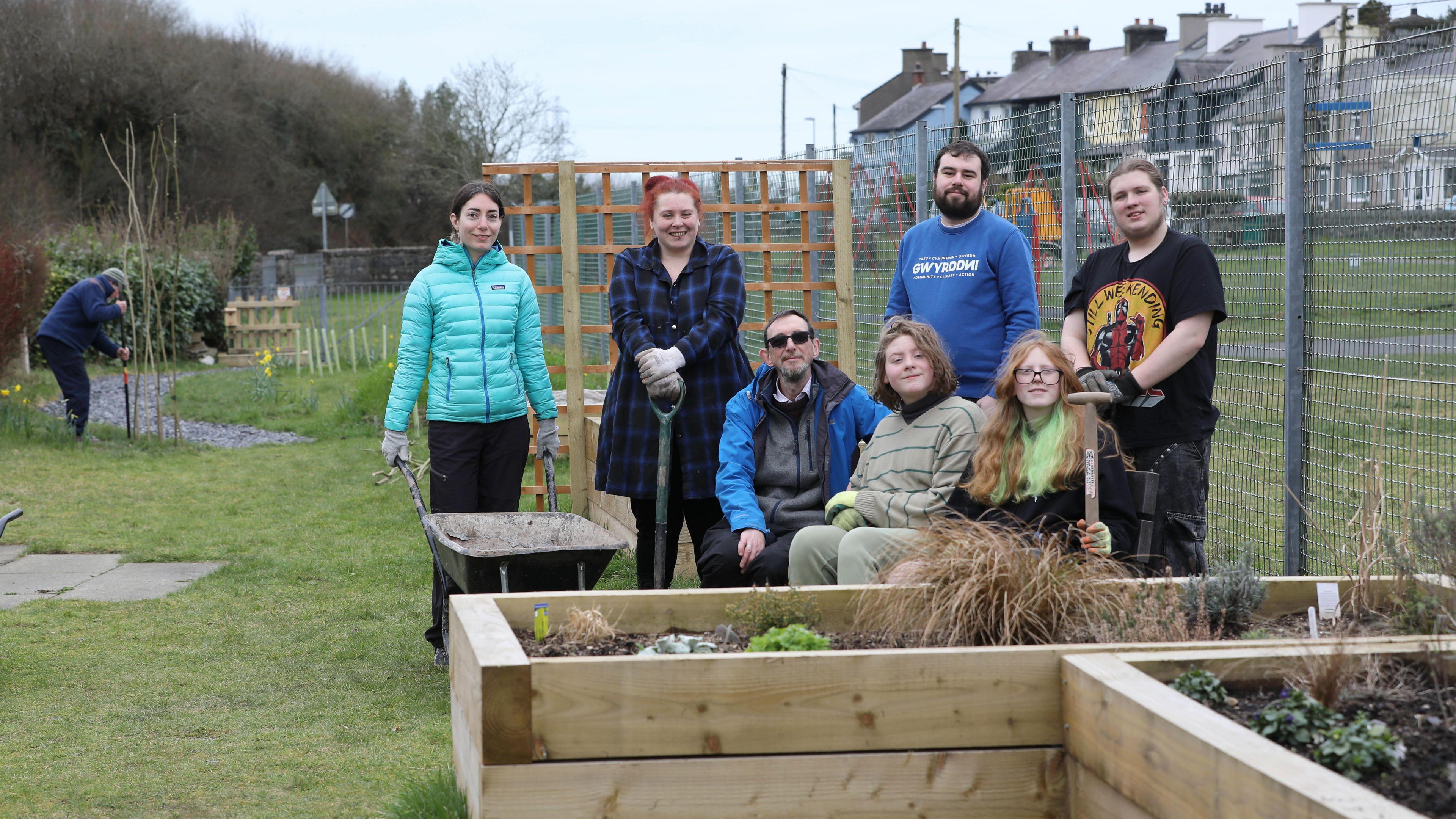Volunteers for the GwyrddNi project in Gwynedd photographed in a community garden. Vegetable planters can be seen in the foreground with a man digging in the background.