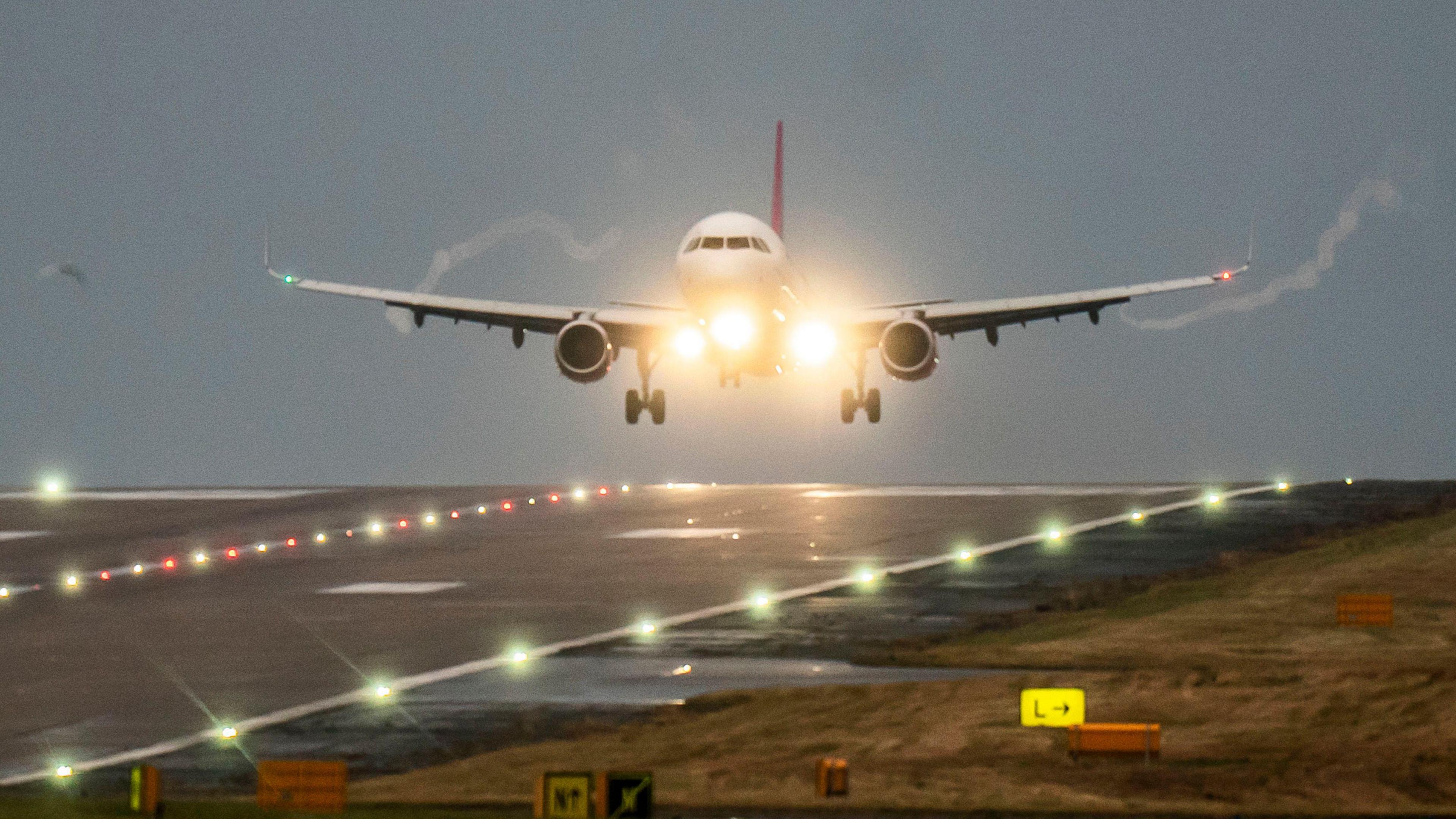 A plane comes in to land at Leeds Bradford Airport in dusky conditions. Lights can be seen at the front of the plane and along the runway.