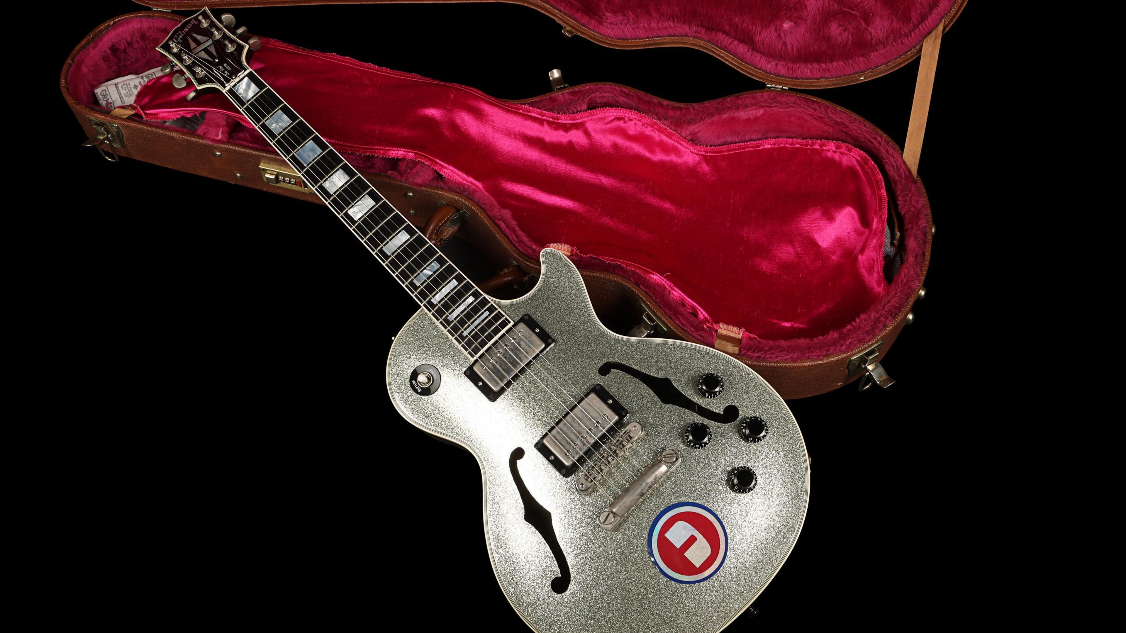 Noel Gallagher's custom Silver Sparkle Gibson Les Paul Florentine is resting next to the guitar case which has a soft red interior