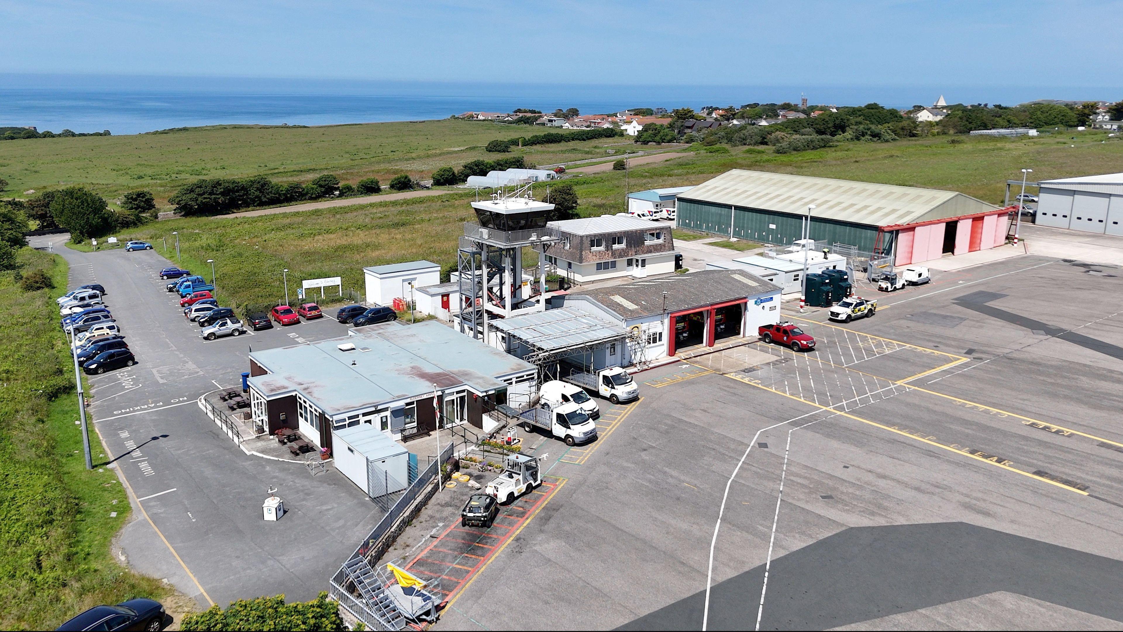 A drone image taken from above of Alderney Airport. It is a large building with a number of vehicles parked next to the runway.