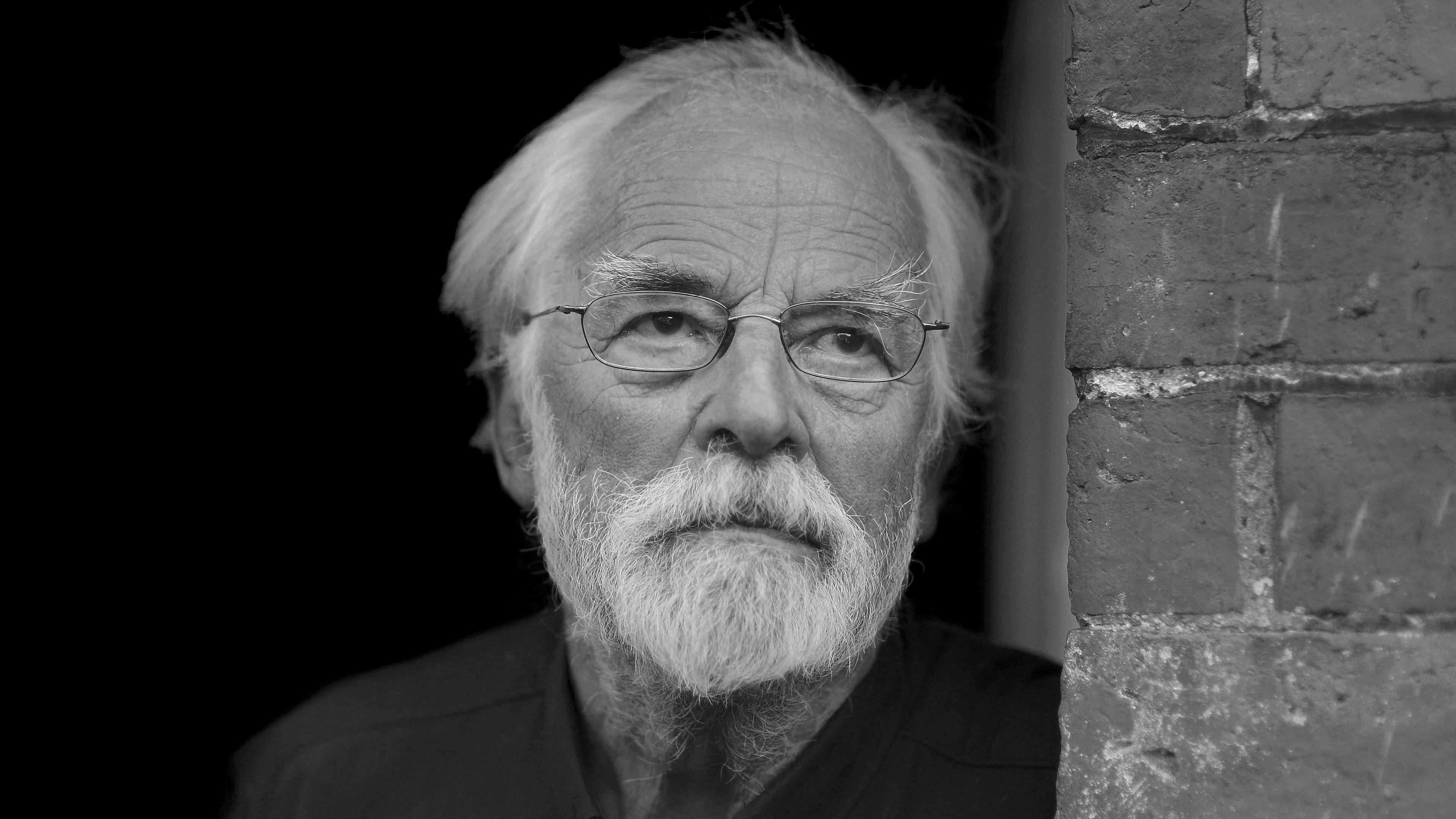 John Marjoram staring into the distance. He is wearing a dark coloured shirt. The image is in black and white.