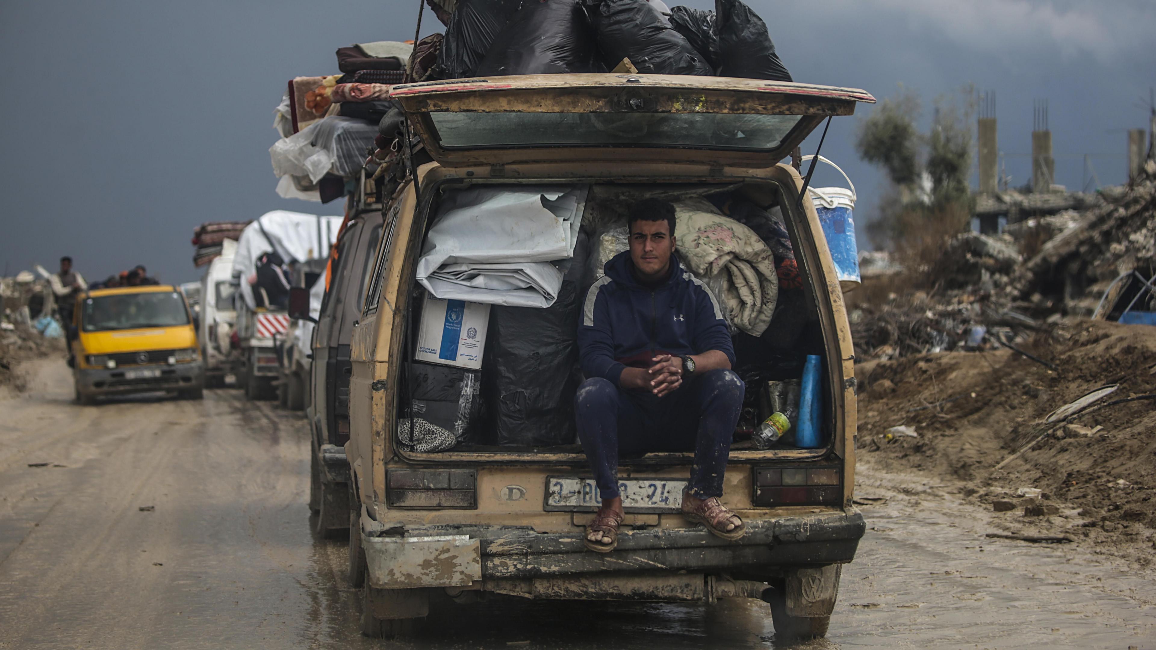 A Palestinian man rides on the back of a van filled with belongings, as displaced people drive from southern Gaza to northern Gaza through the Netzarim Corridor (12 February 2025)