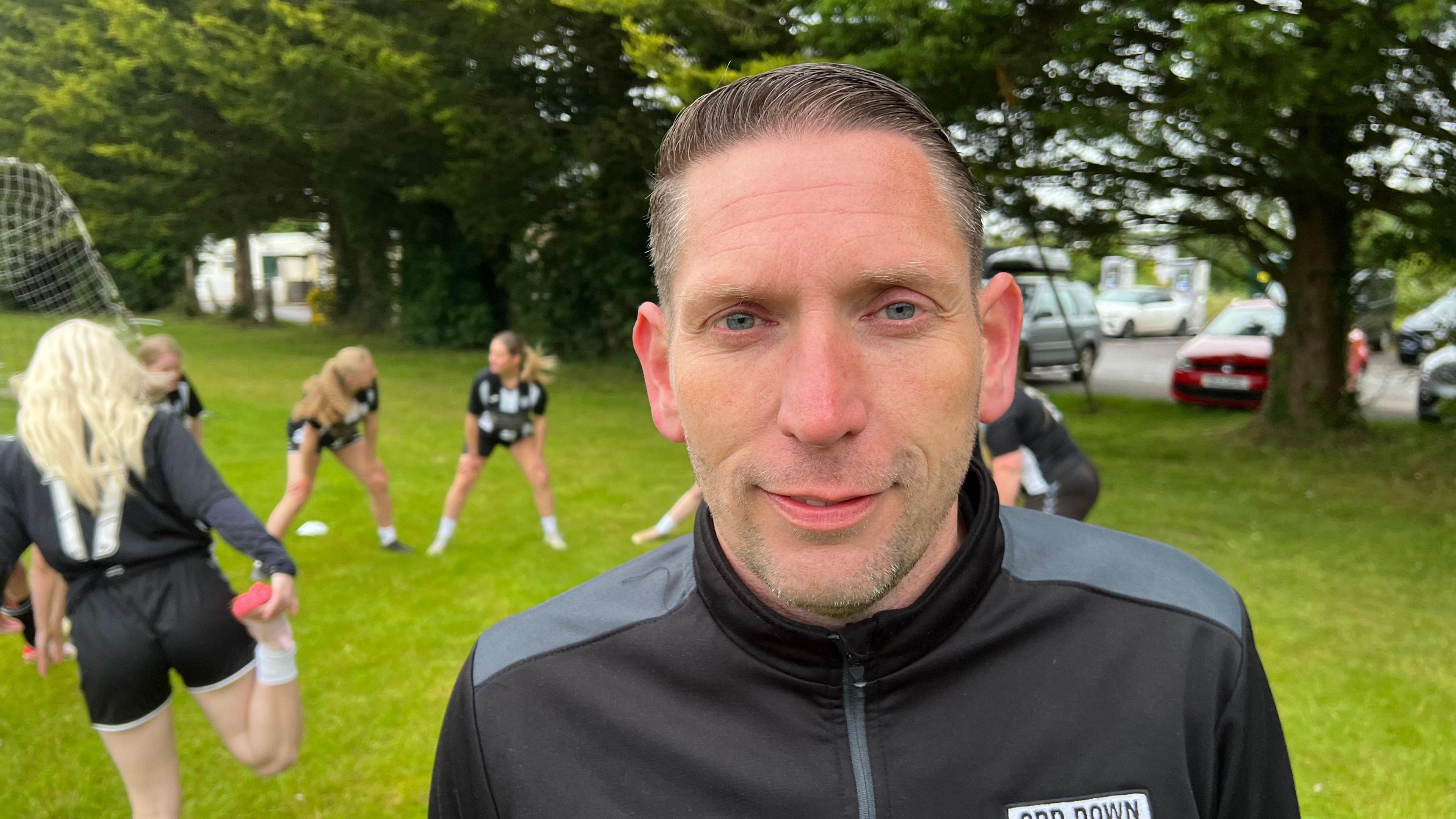 Ross Andrews looking at the camera with Odd Down FC players training behind him