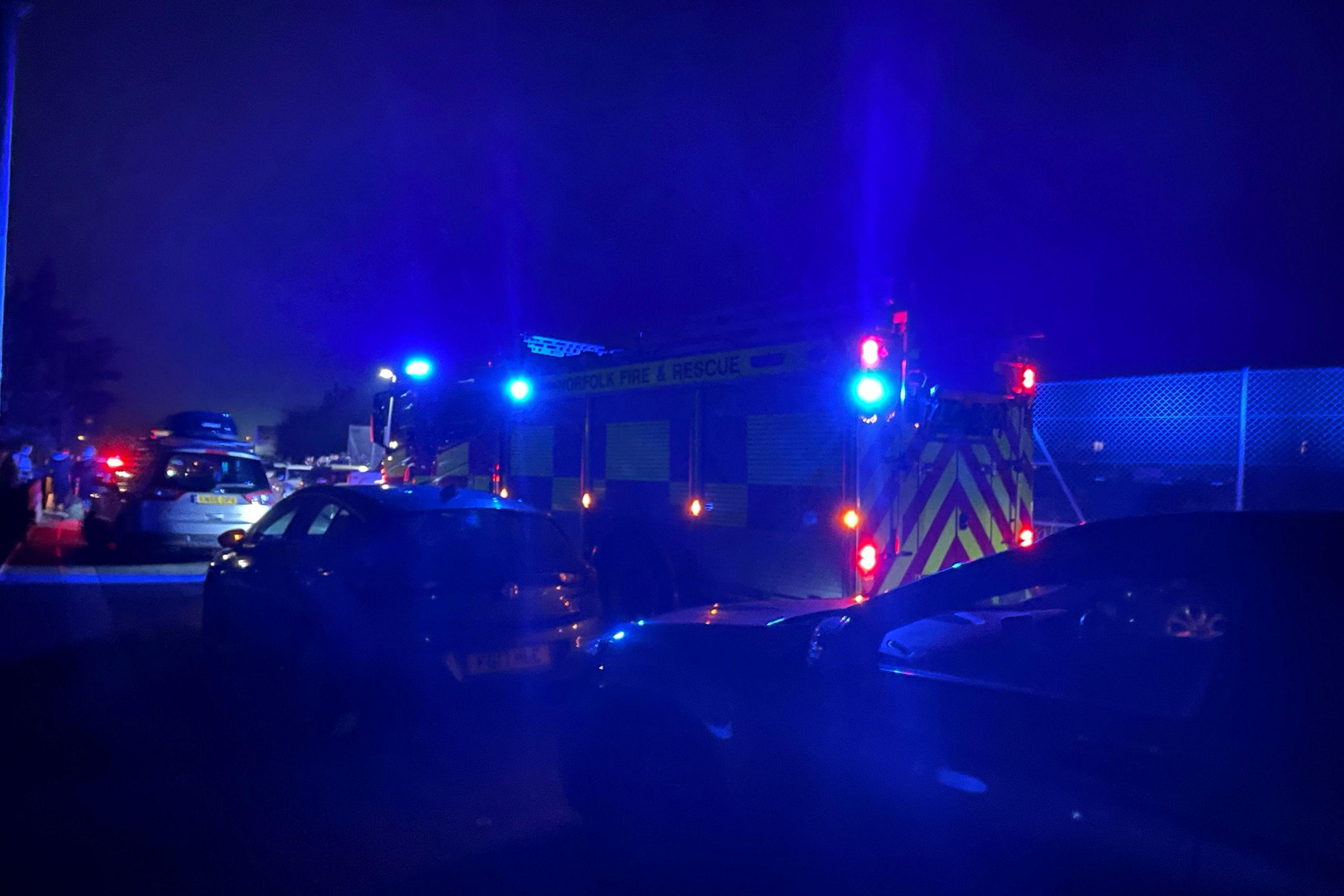 A fire truck, with blue lights on, held up in queueing traffic. It is dark.