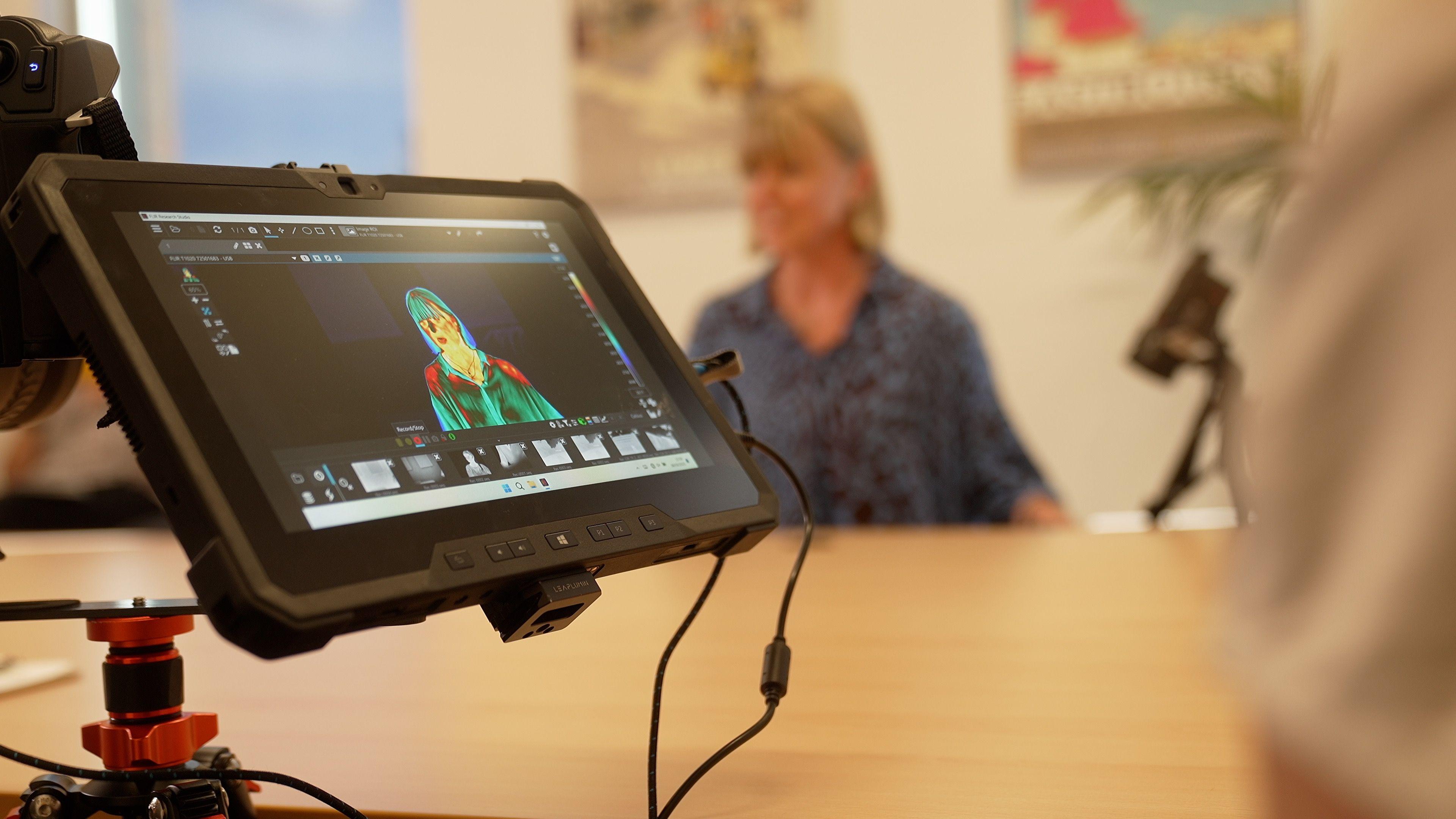 a video camera viewfinder shows the correspondent's thermal image while the correspondent herself is blurred out in the background.