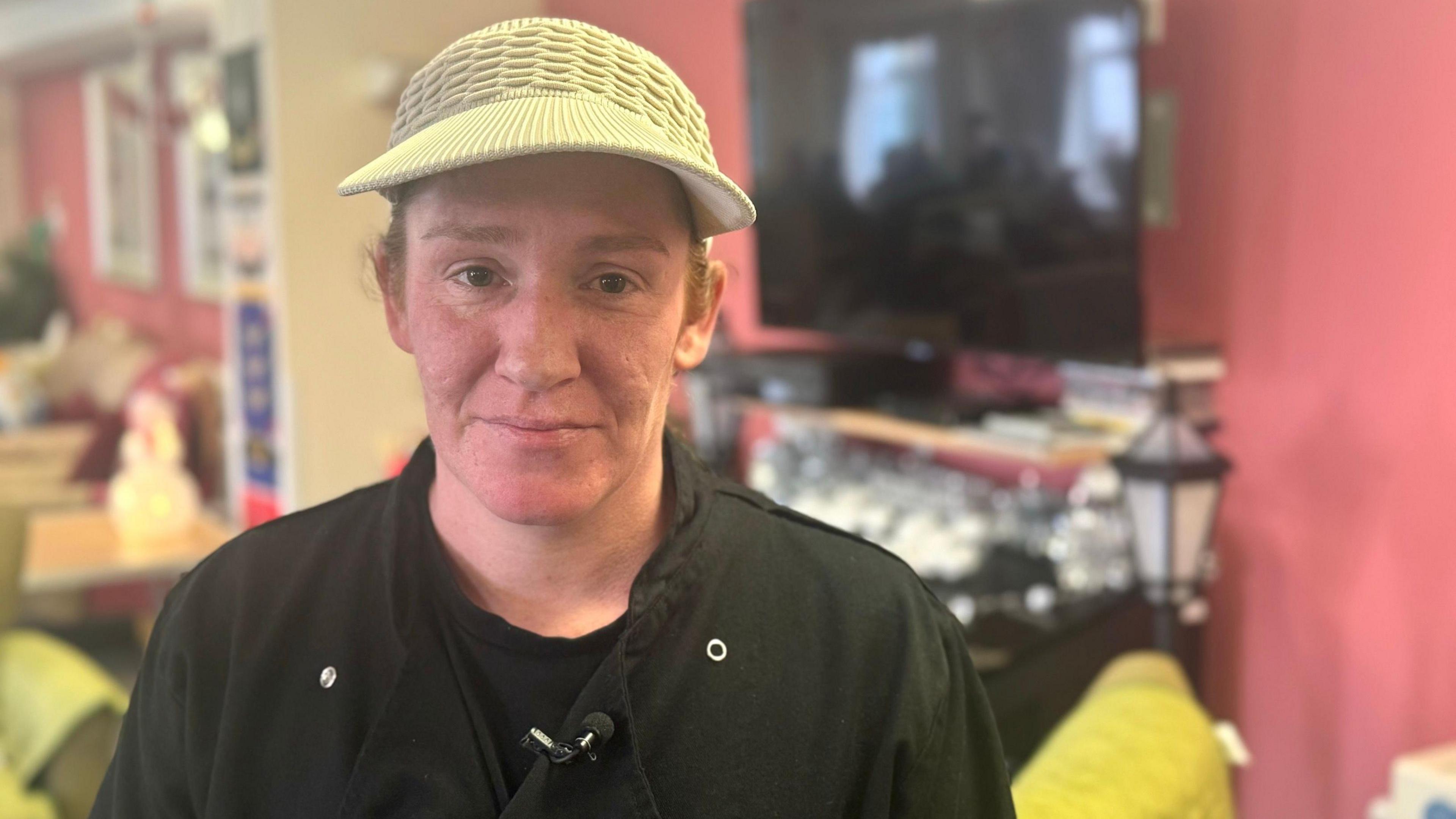 Volunteer Fran is standing in the cafe wearing a cream coloured hat and a black top