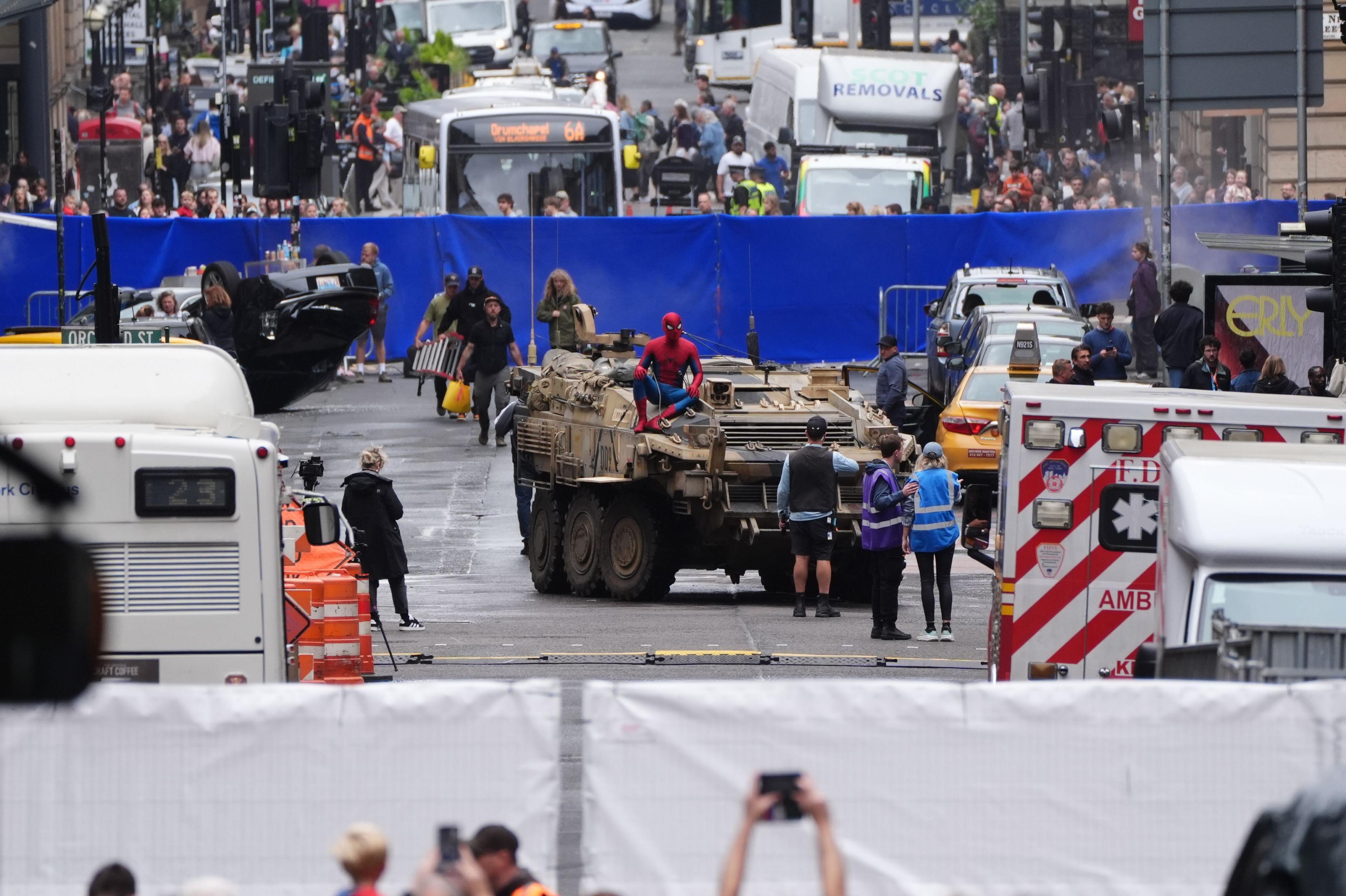 A street scene with Spiderman on top of a tank. Behind that is a blue screen, with a Glasgow bus beyond that