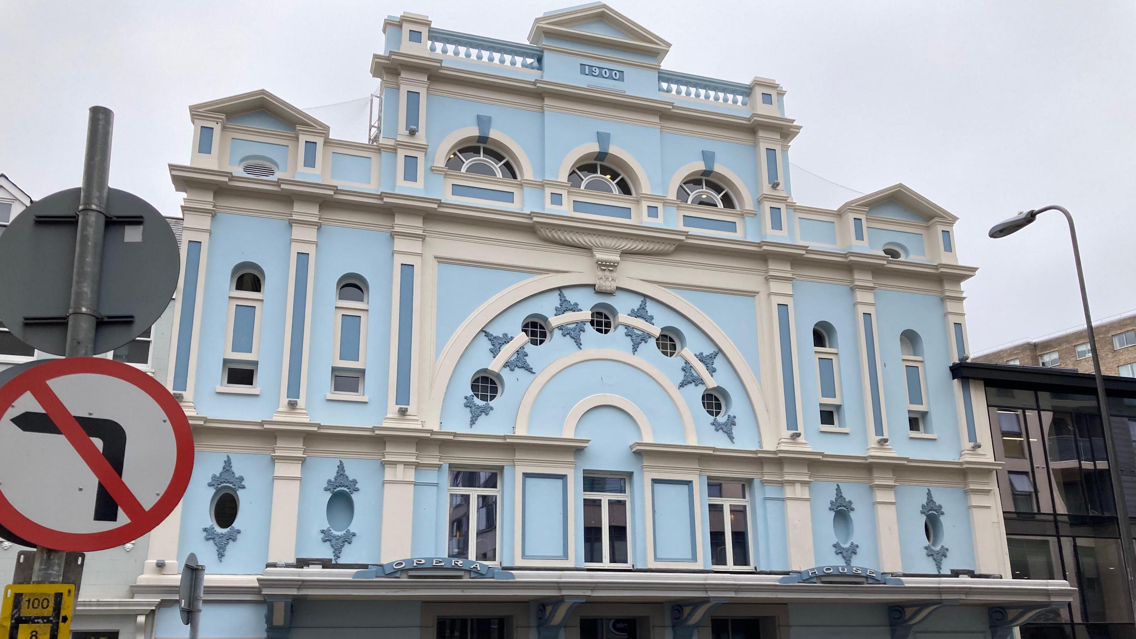 Jersey Opera House exterior showing a blue and white building with patterns. In the foreground is a street sign with a no left turn symbol.