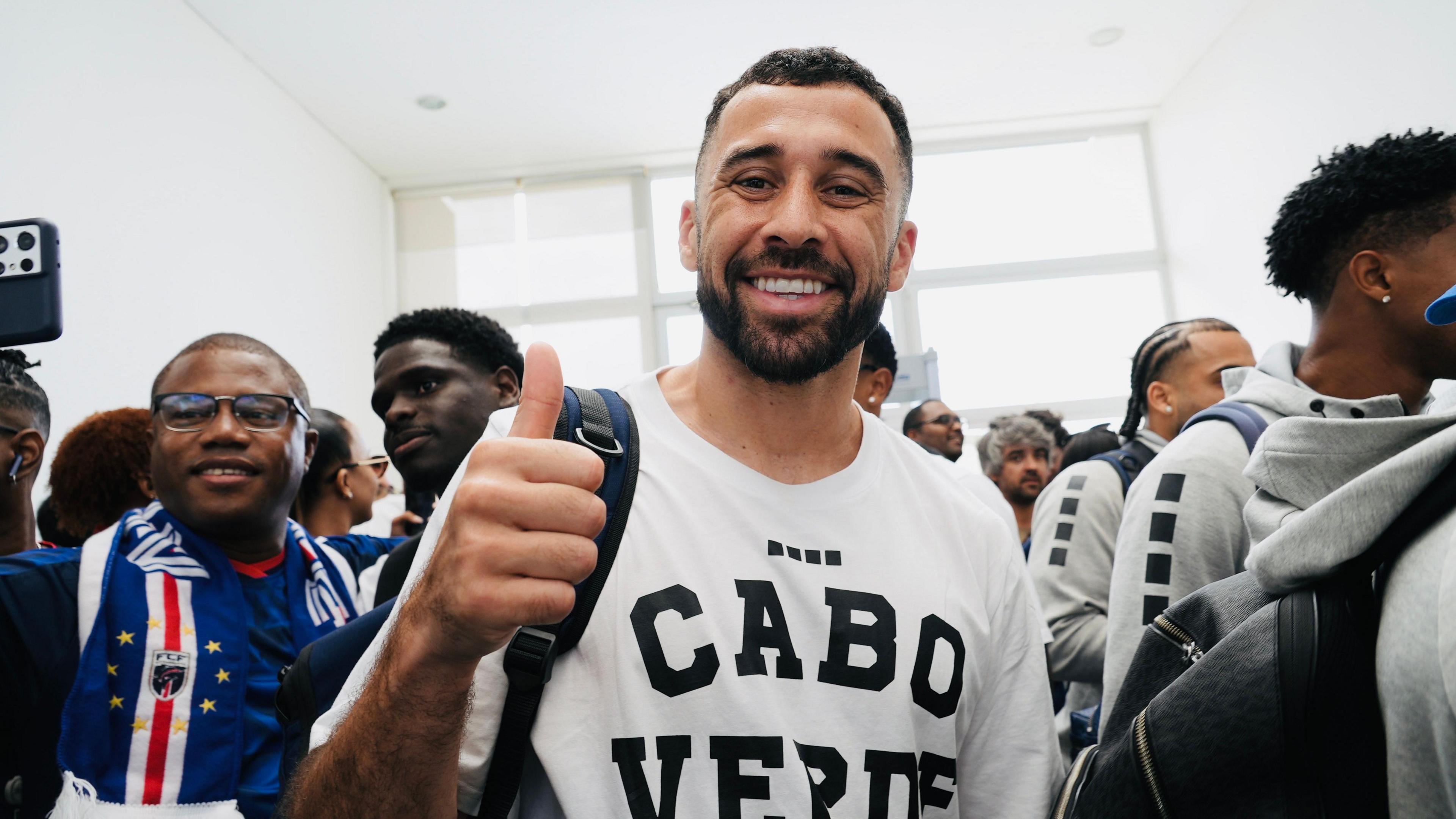 Pico Lopes smiles at the camera, wearing a white t-shirt emblazoned with the words