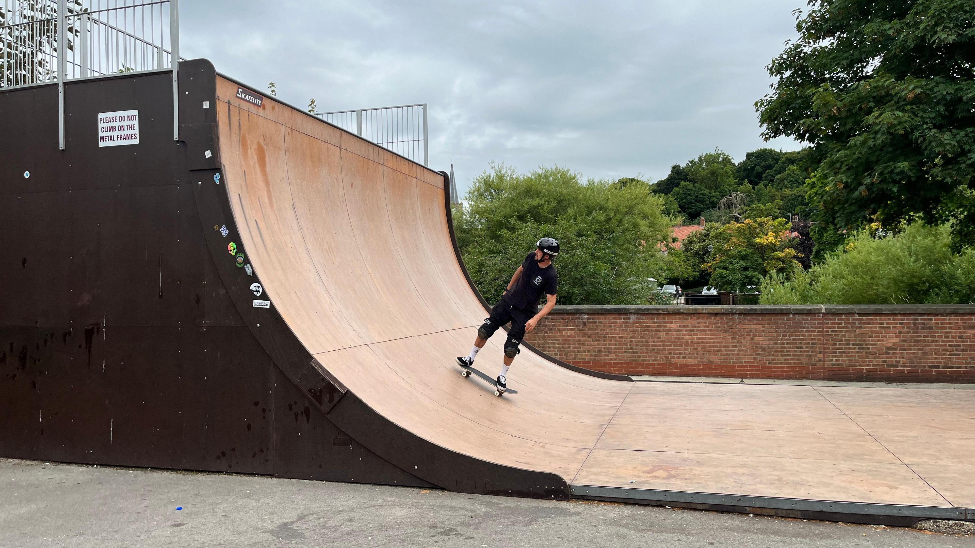 Ryan Swain on skateboard on large wooden half pipe