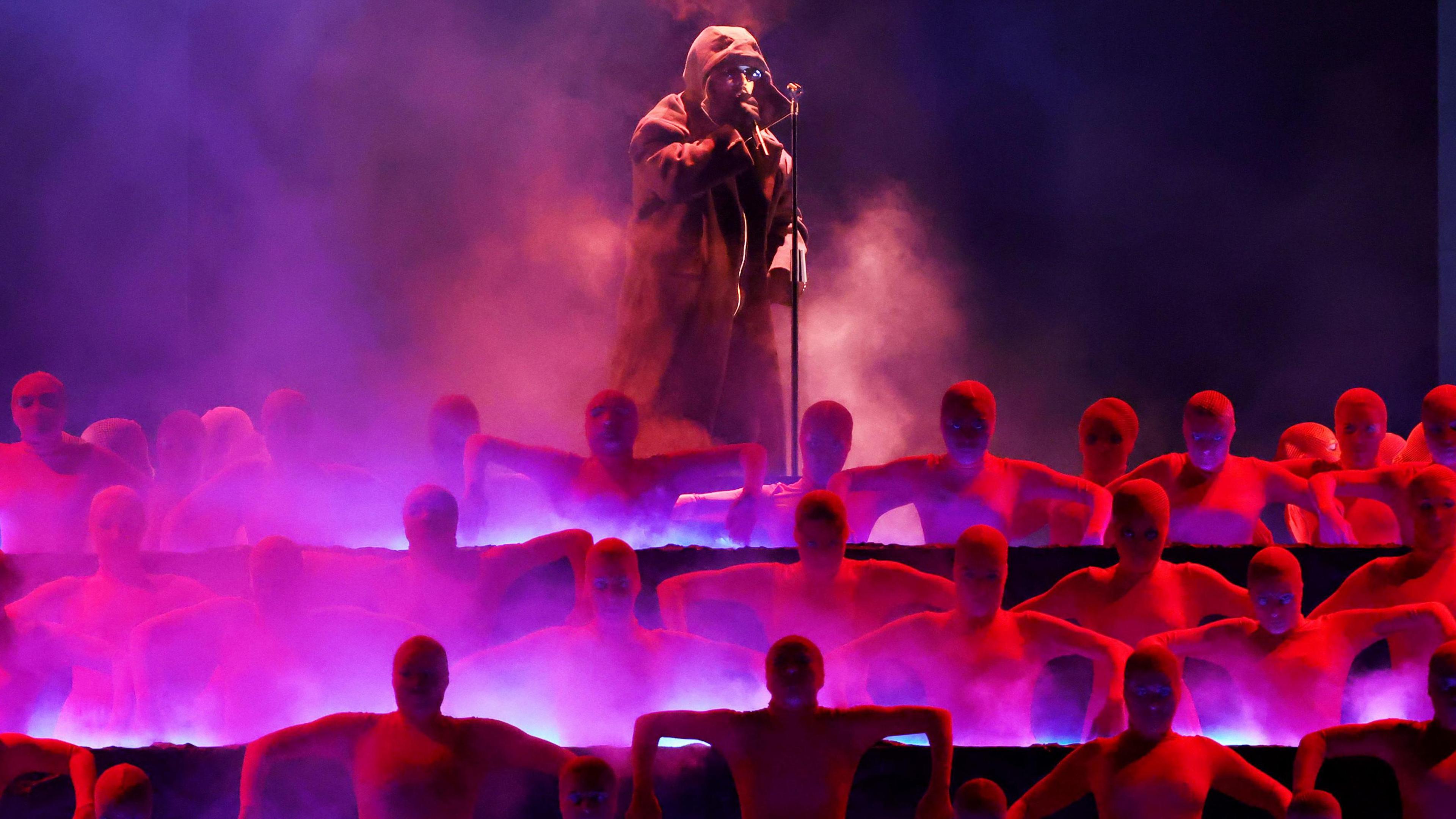 The Weeknd pictured on-stage in a hooded jacket, while raised above a group of dancers