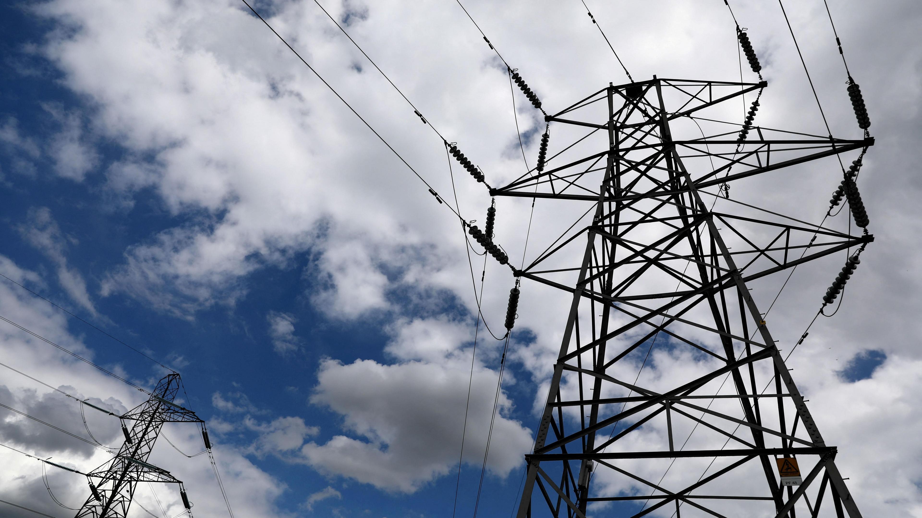 Two pylons viewed from below, against a blue sky full of white clouds.