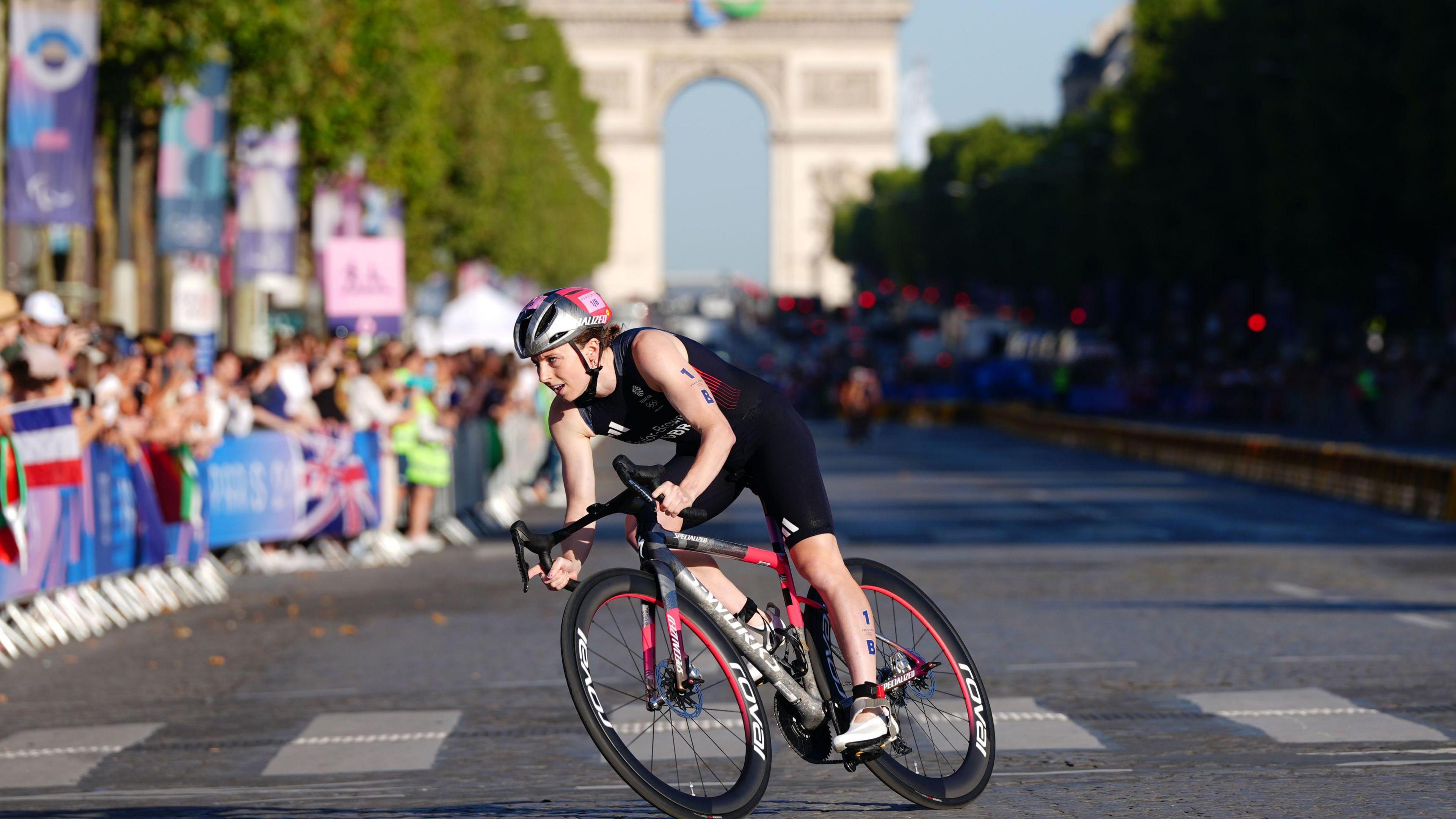 Team GB's Georgia Taylor-Brown riding a bike through Paris with crowds lining the street and the Champs-Élysées in the background.