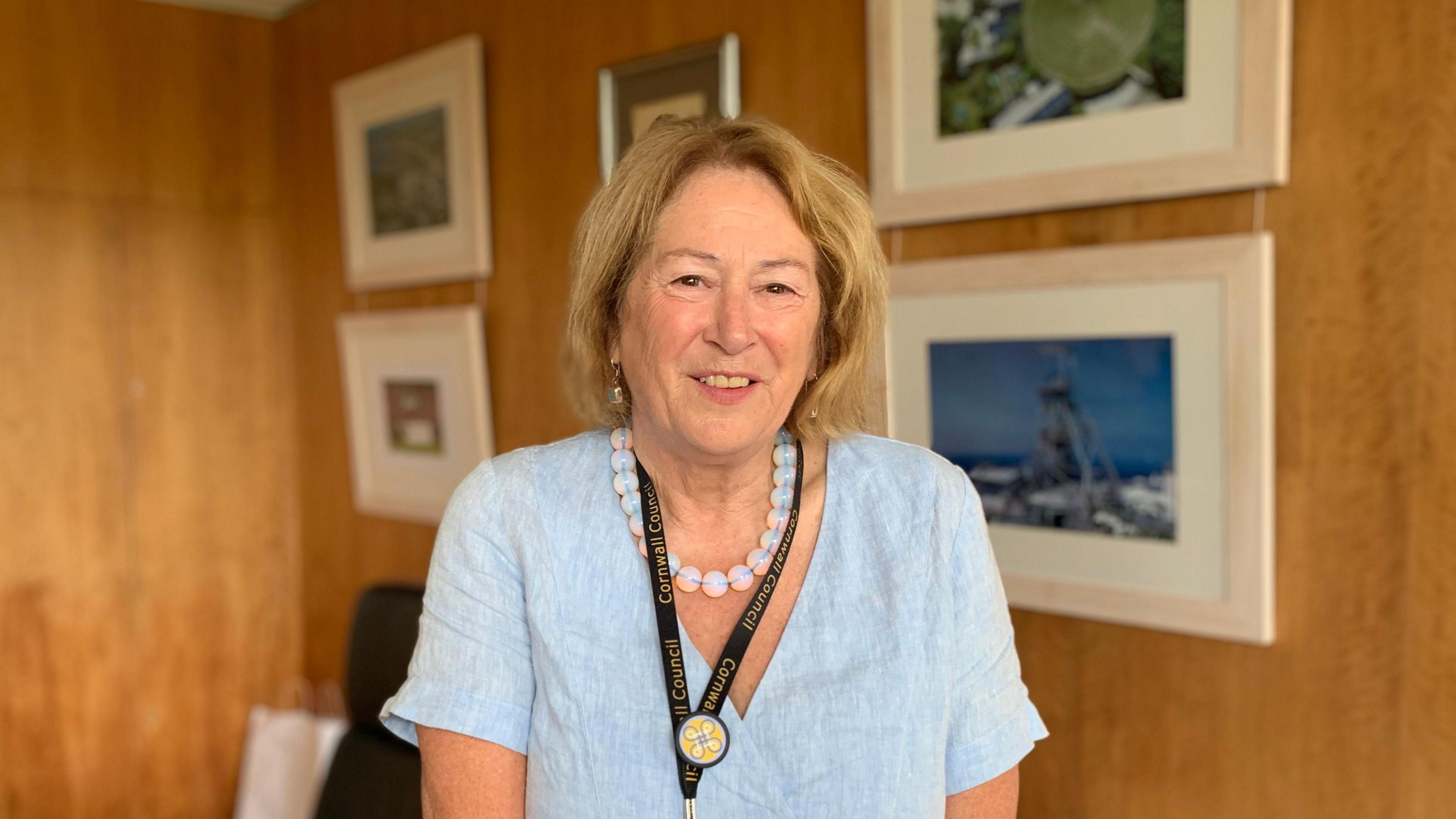 Linda Taylor wearing a light blue v-necked top with a beaded necklace and a black Cornwall Council lanyard. She has short, shoulder-length hair and is smiling at the camera.