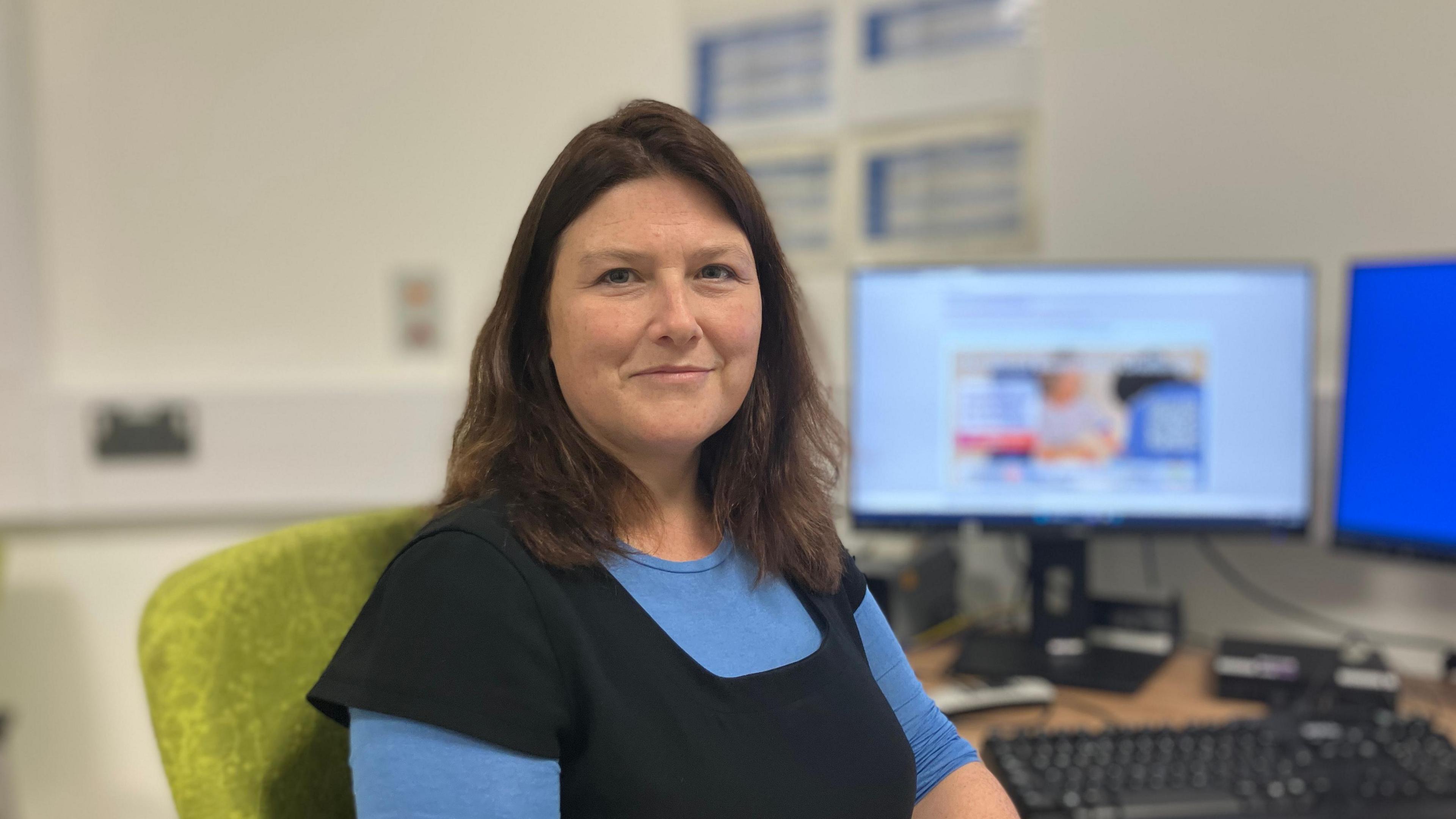 A female doctor/scientist with dark hair is sitting in a hospital consulting room