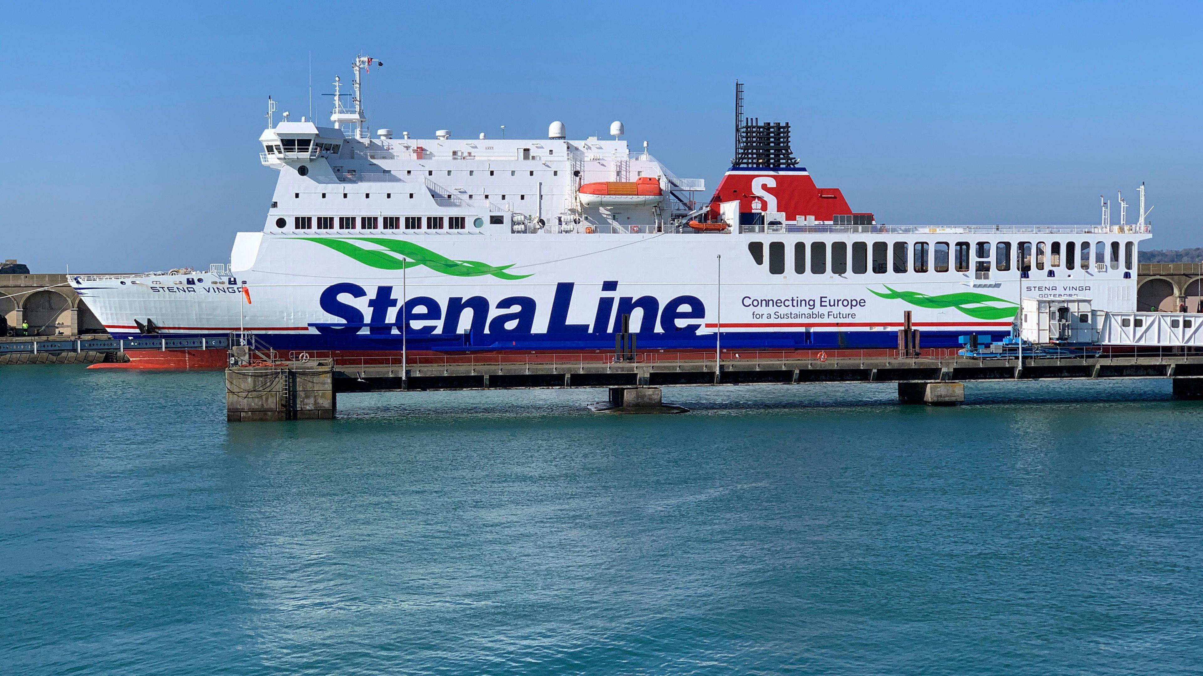 A large white ferry is coming alongside the stone quay on a blue sea on a blue sky day. Printed along its port side is Stena Line Connecting Europe for a Sustainable Future.