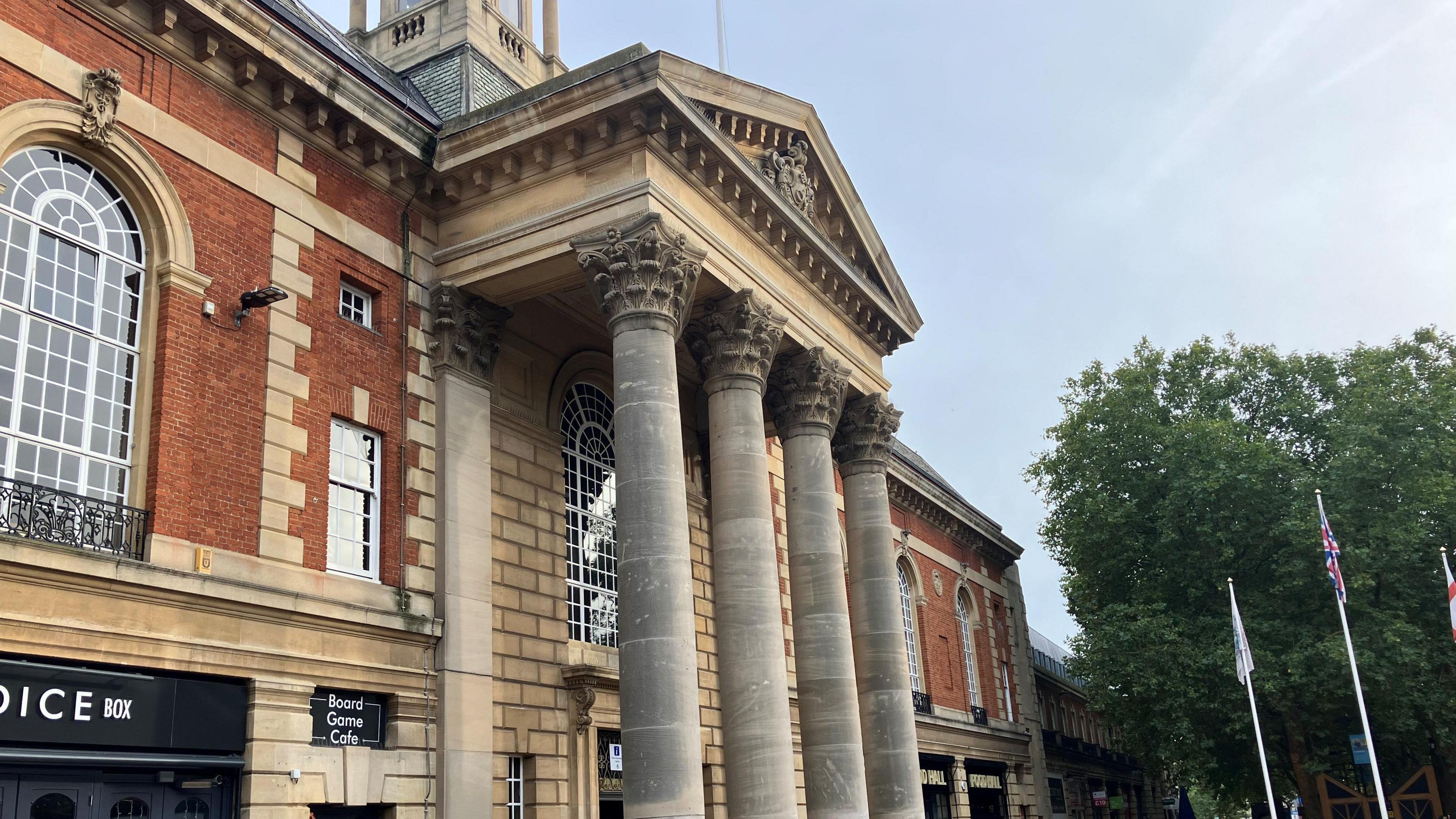 Peterborough's Town Hall- a two storey brick building with four stone columns supporting an ornate canopy at its entrance.