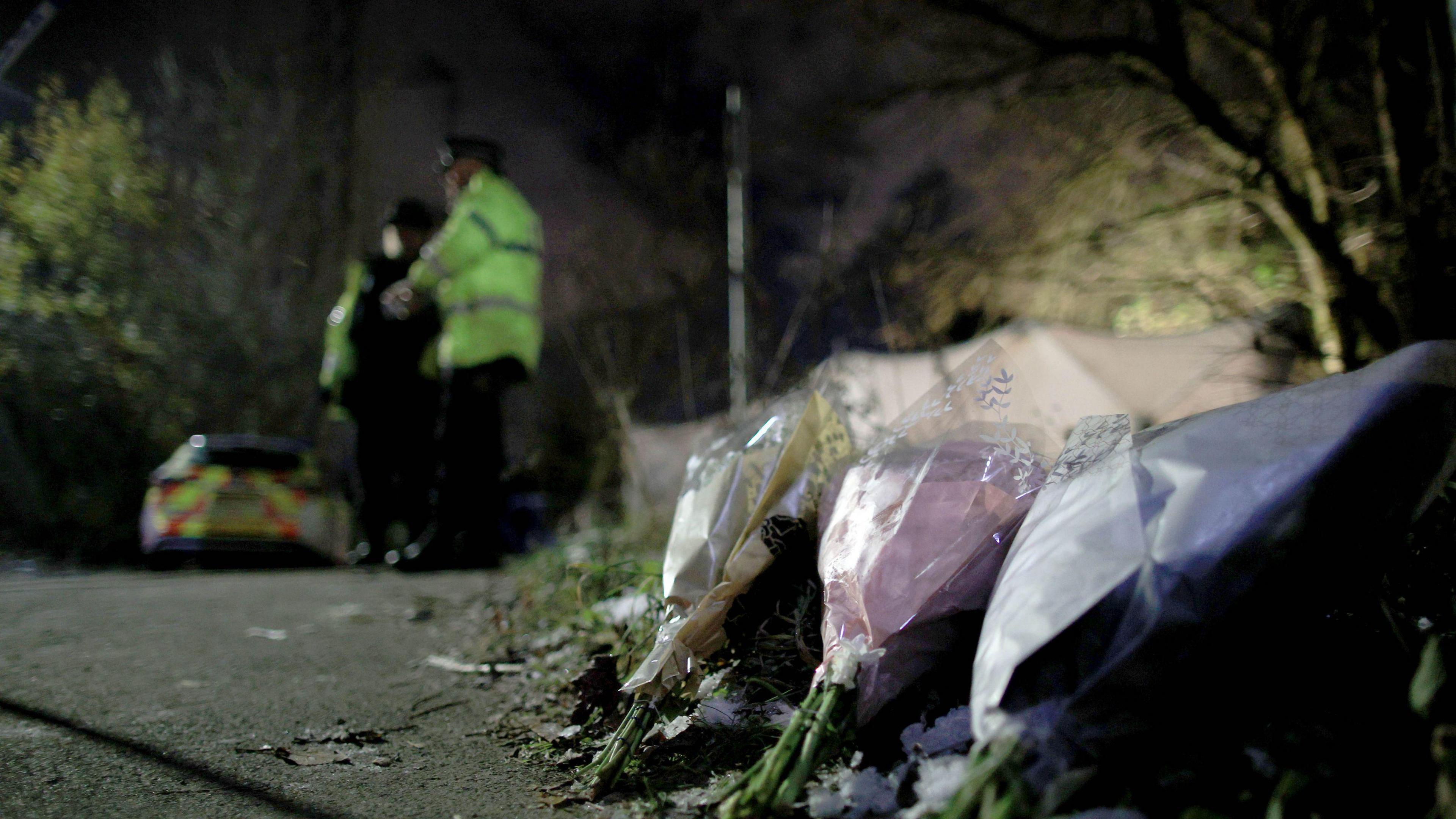 Bouquets of flowers left on Ravenscraig Road, near Ashtons Field in Salford, Greater Manchester, where the remains of a baby were found in a field. Police officers and a police car are in the background of the photograph.