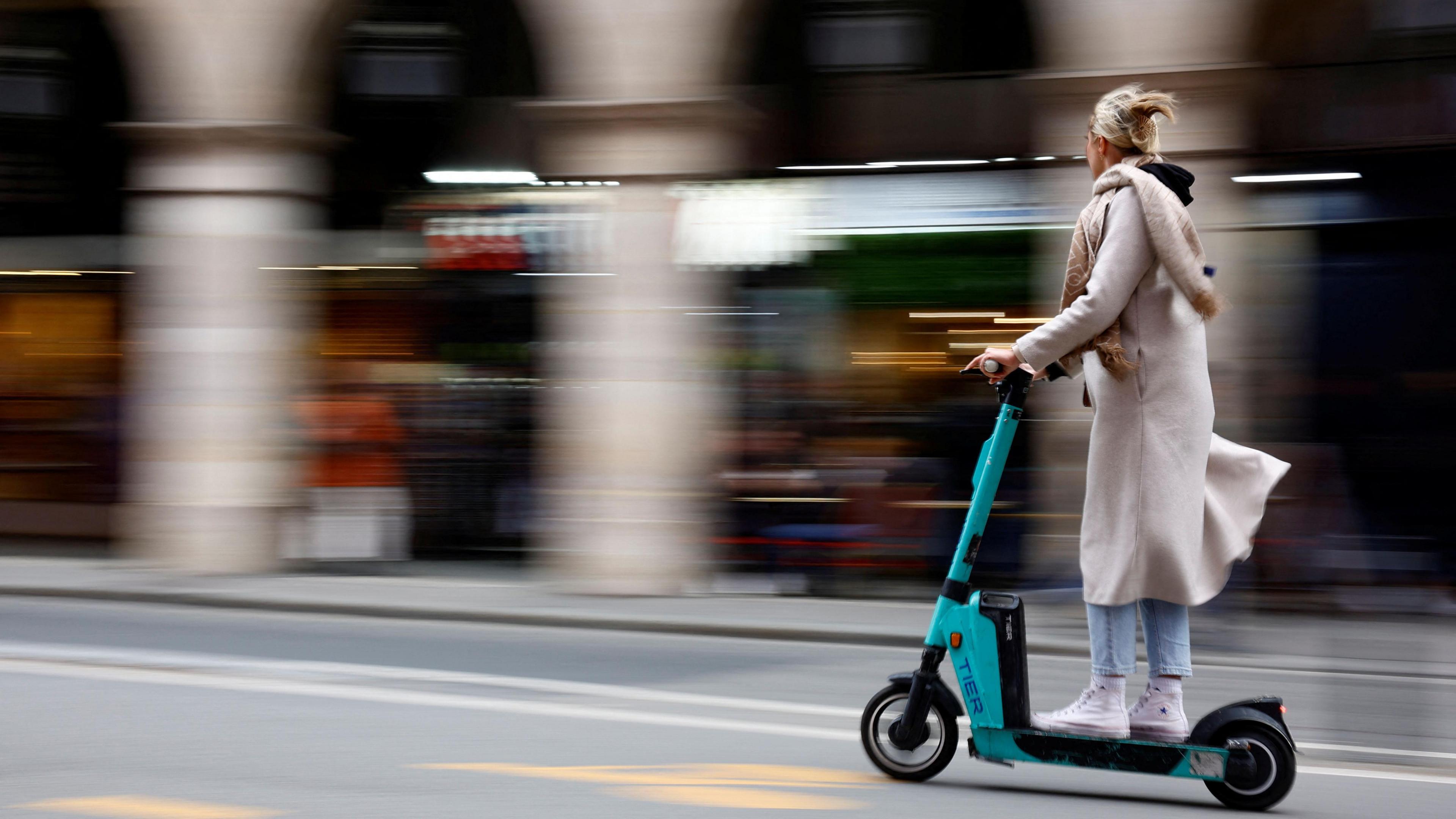 A woman riding a Tier-branded e-scooter on a road