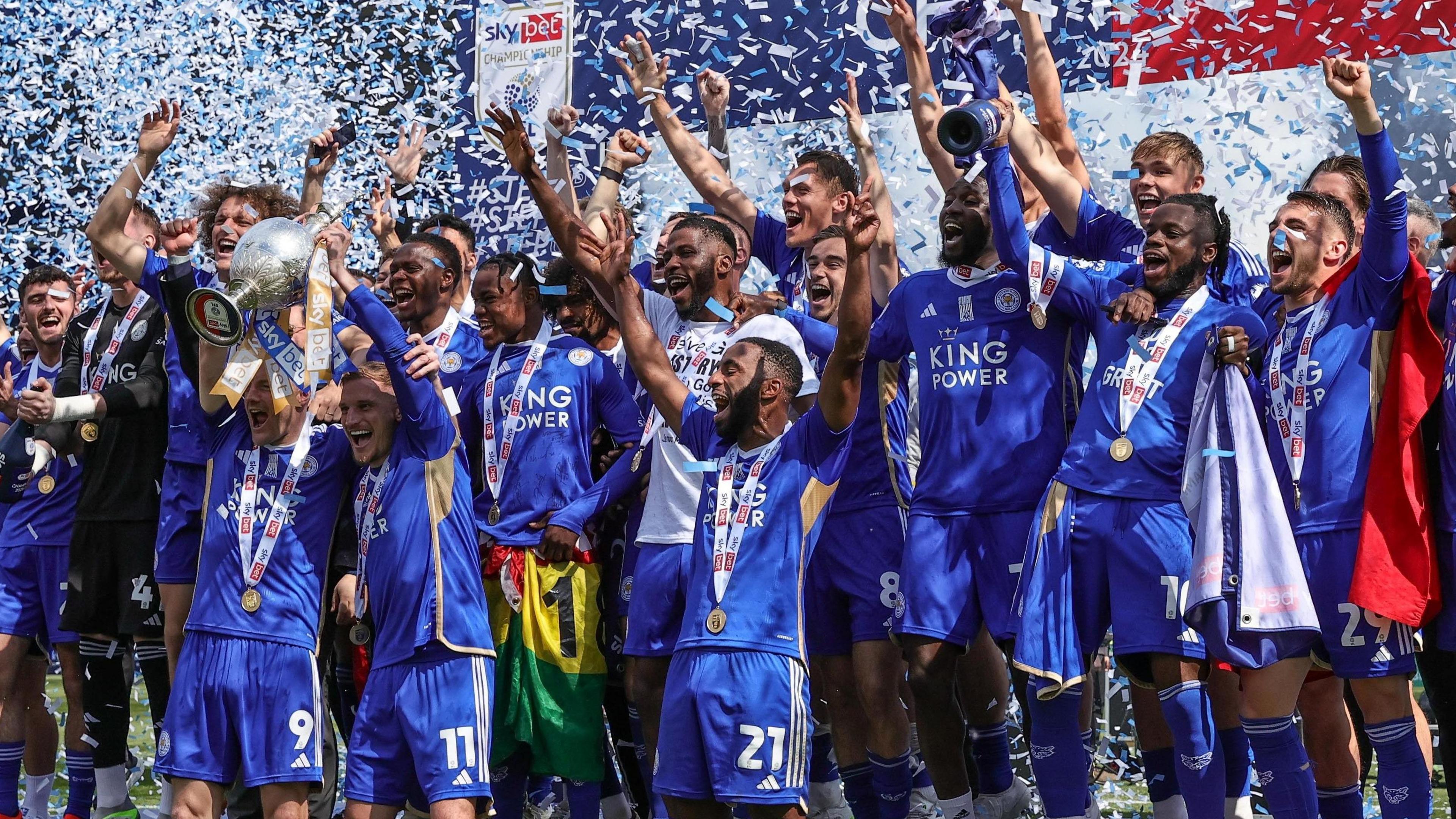 Leicester City's squad lift the Championship trophy together as ticker tape falls down behind them