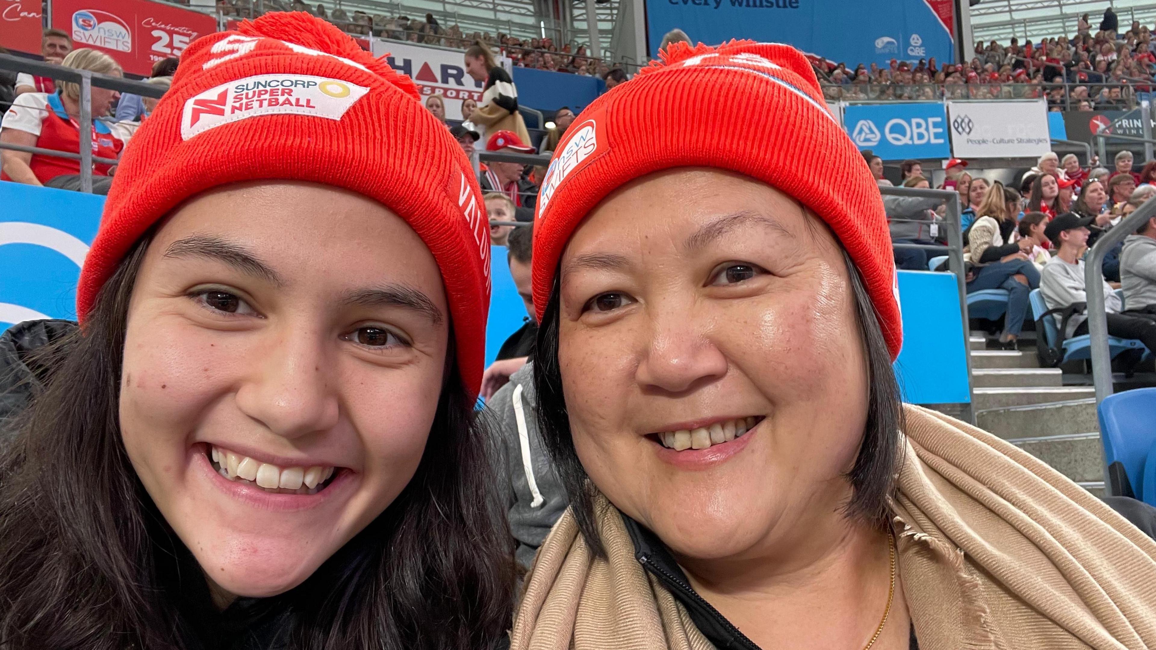 Sophie Fawns with her mother, Maureen, both smiling and wearing NSW Swifts red woolly hats