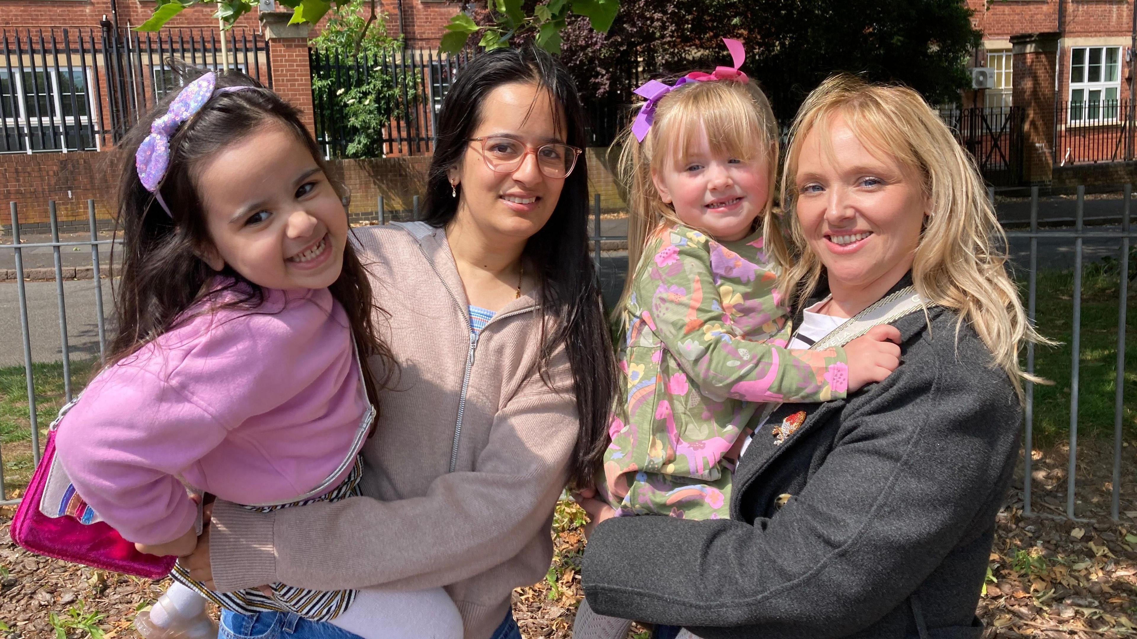 Two mums and their daughters are smiling for the photo in a park near the Saffron pre-school in Leicester. 