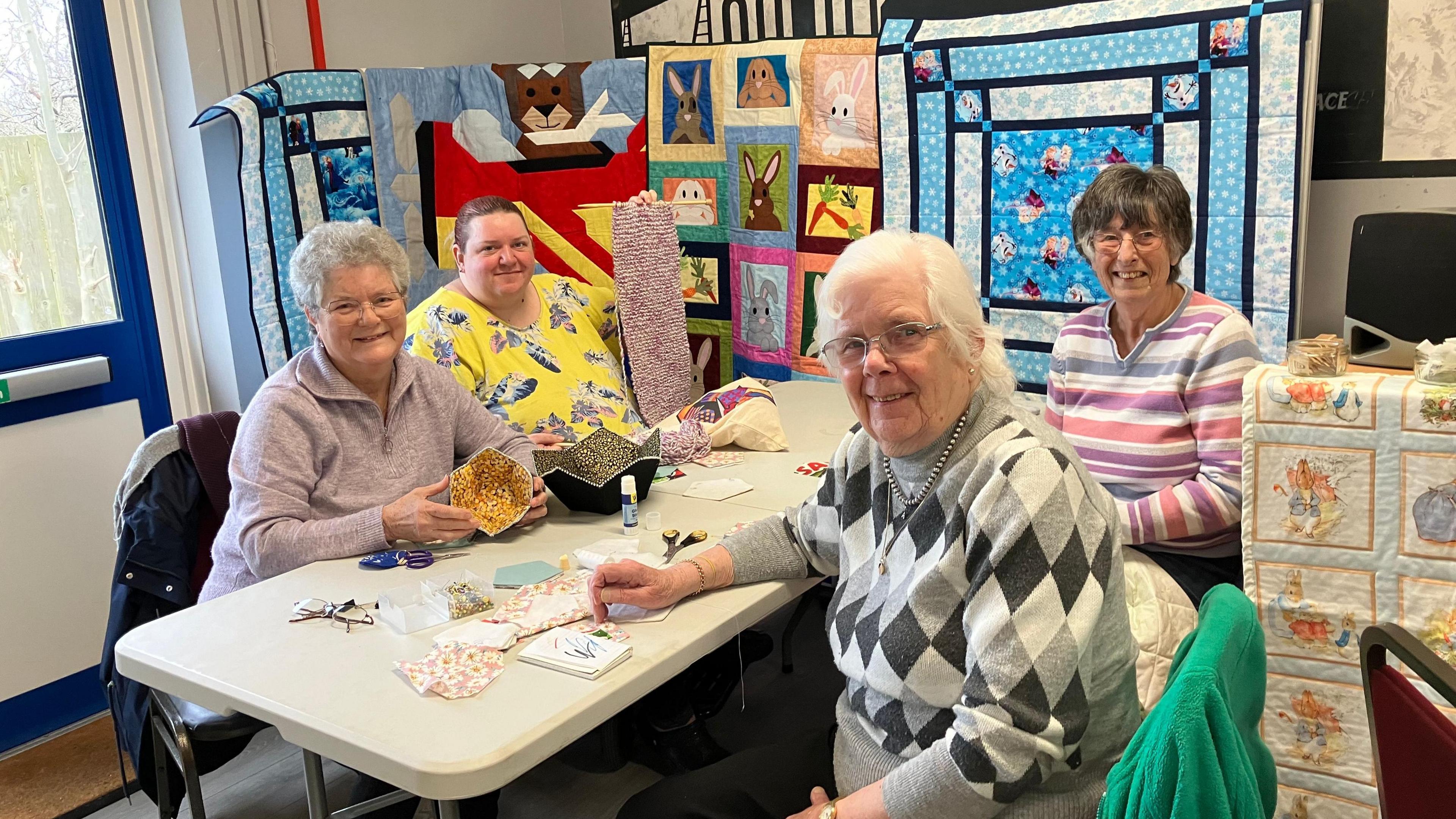 Four members of the sewing club making various items. The women are sitting around a table.