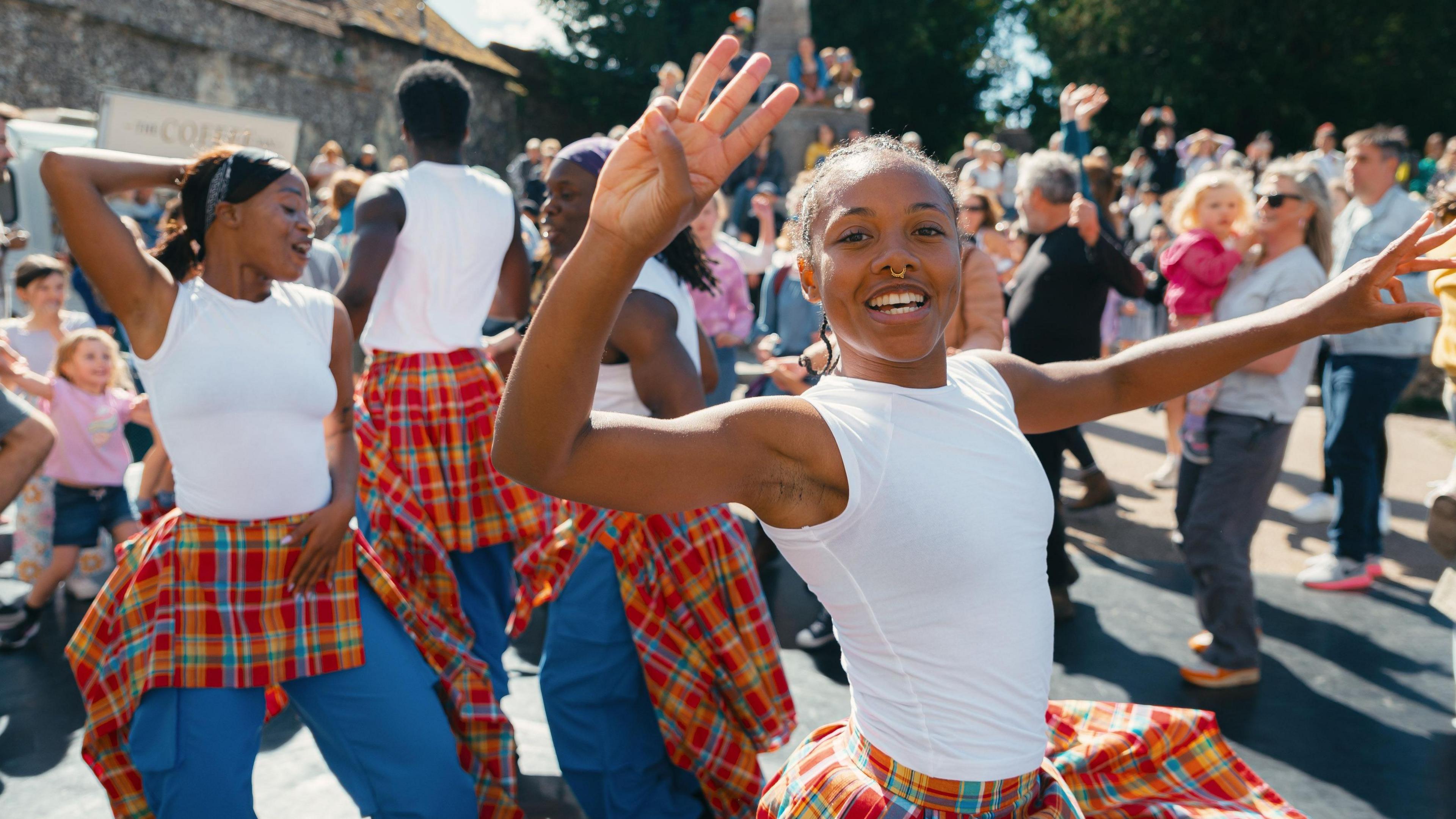 A group of young dancers perform in the street watched by a crowd of people.