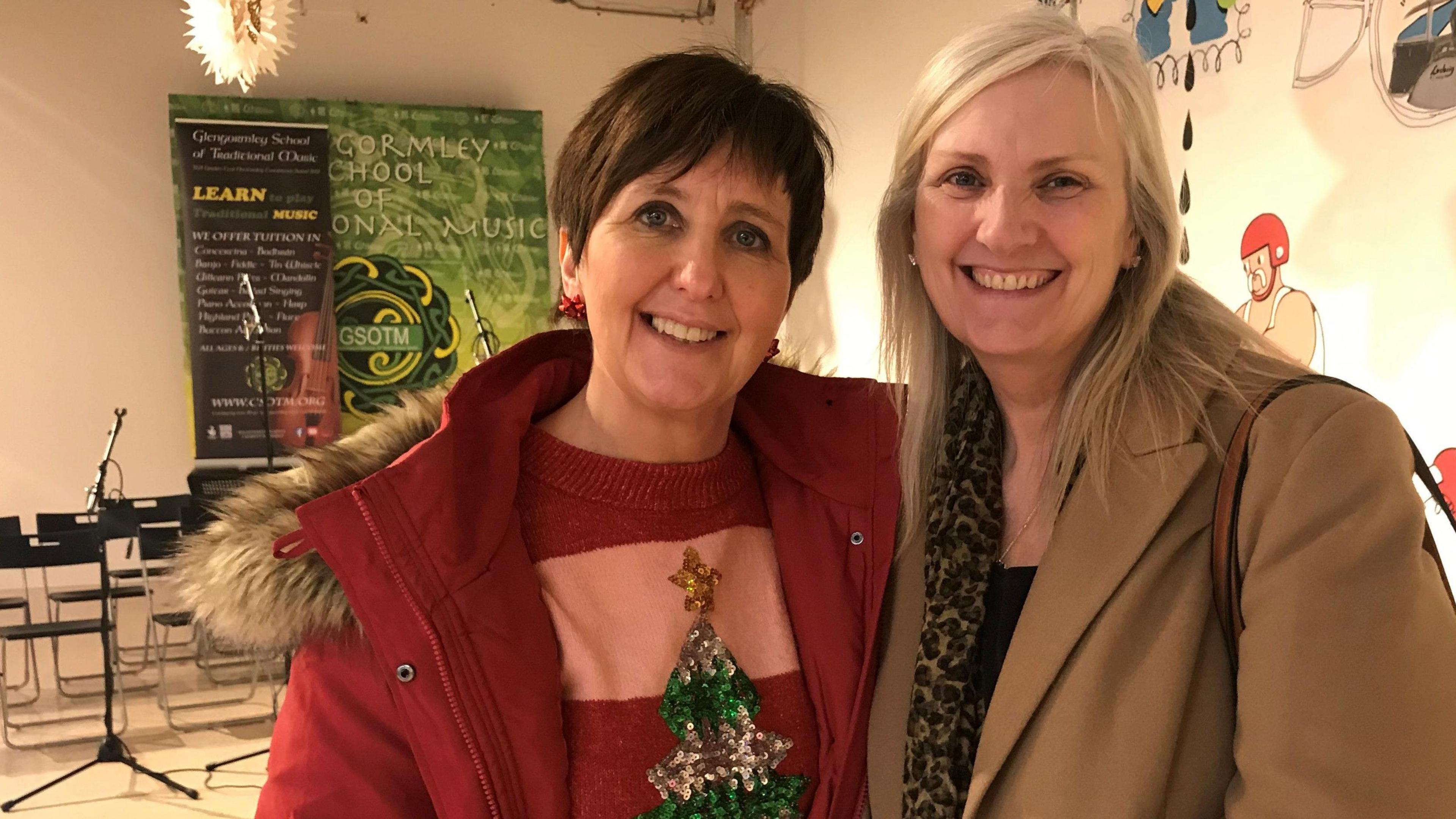 Sharon Cauldwell and Alison McKeown in 2 Royal Avenue.  Sharon has short, dark hair and is wearing a red overcoat and a striped Christmas jumper.  Alison has long, straight blonde hair and is wearing a camel-coloured coat and a animal print scarf. 