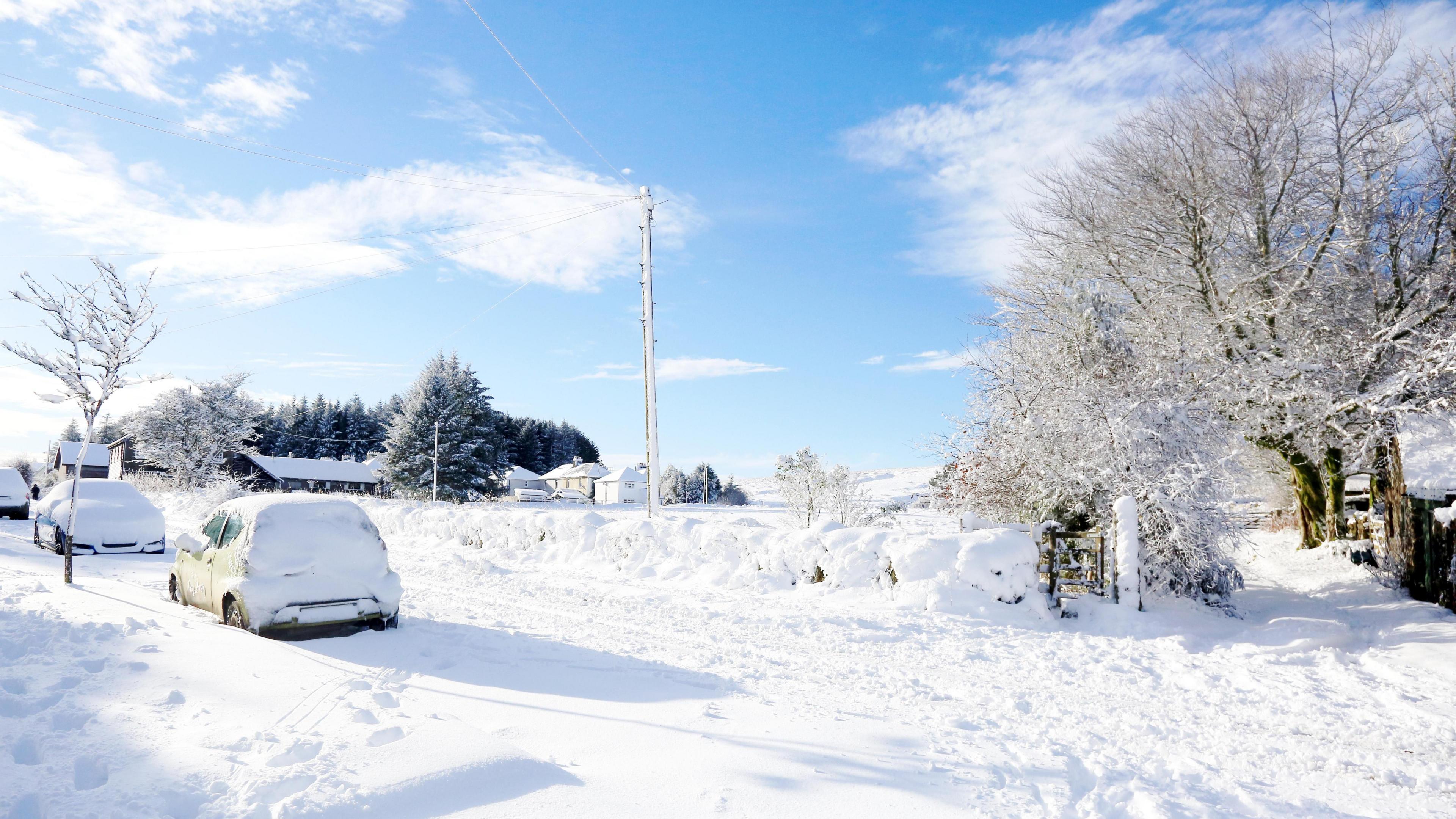 Parked cars covered in snow on a snowy road in Devon