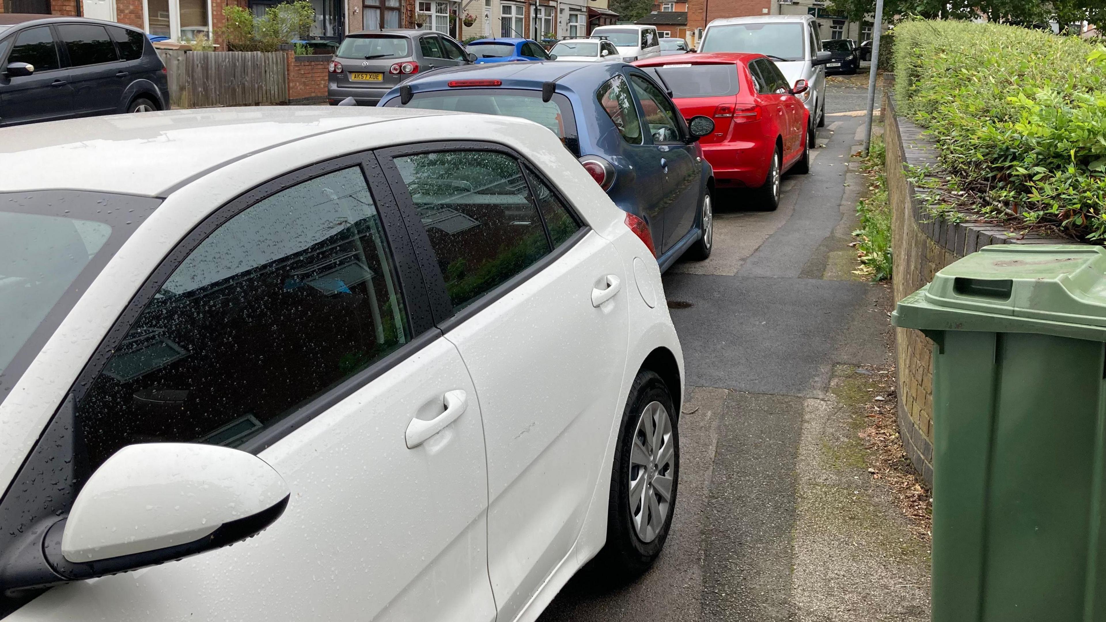 A street lined with a number cars parked on the pavement.