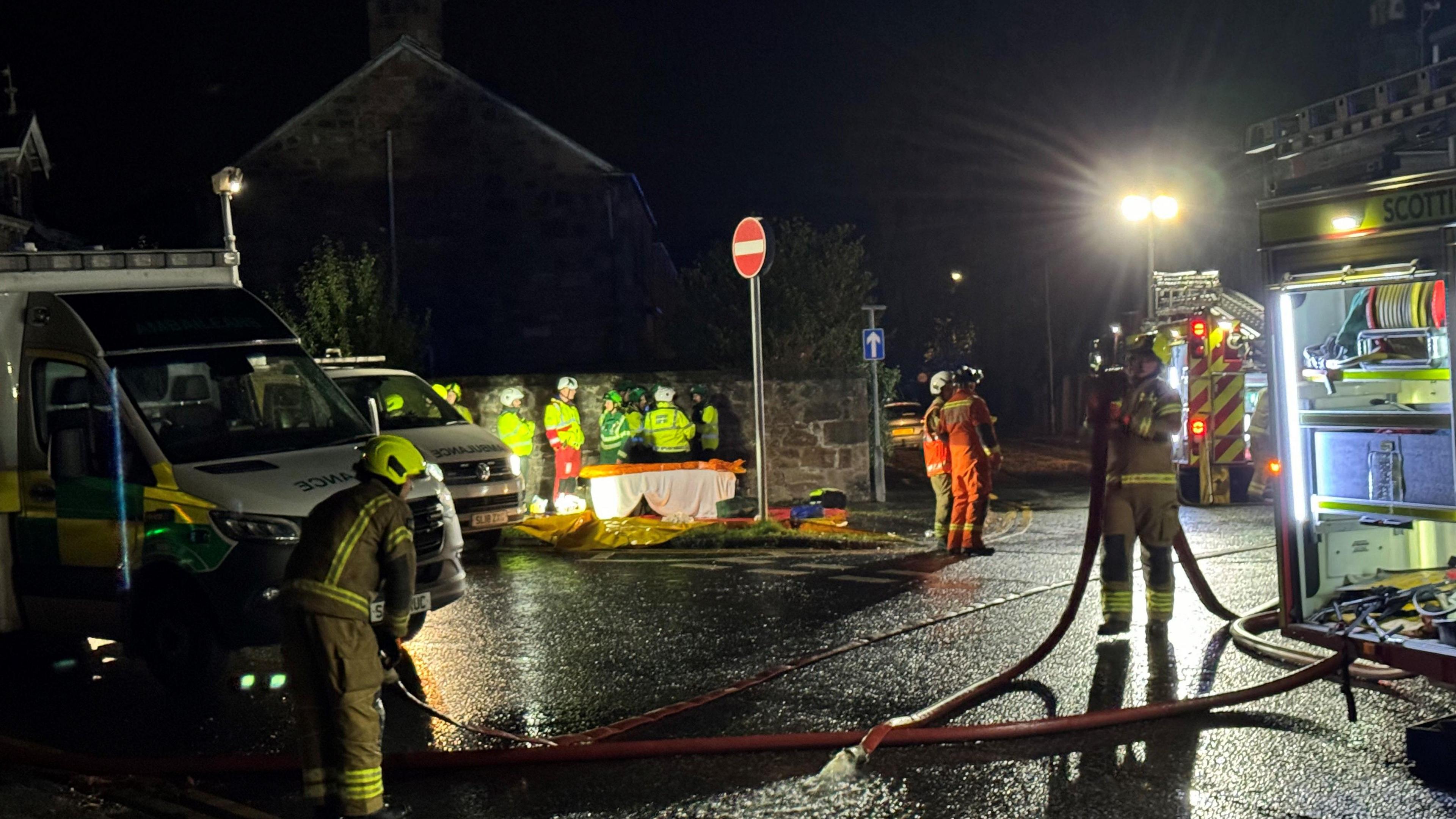 Firefighters with a hose standing alongside appliances and other emergency workers at the scene of the explosion in Kellie Place