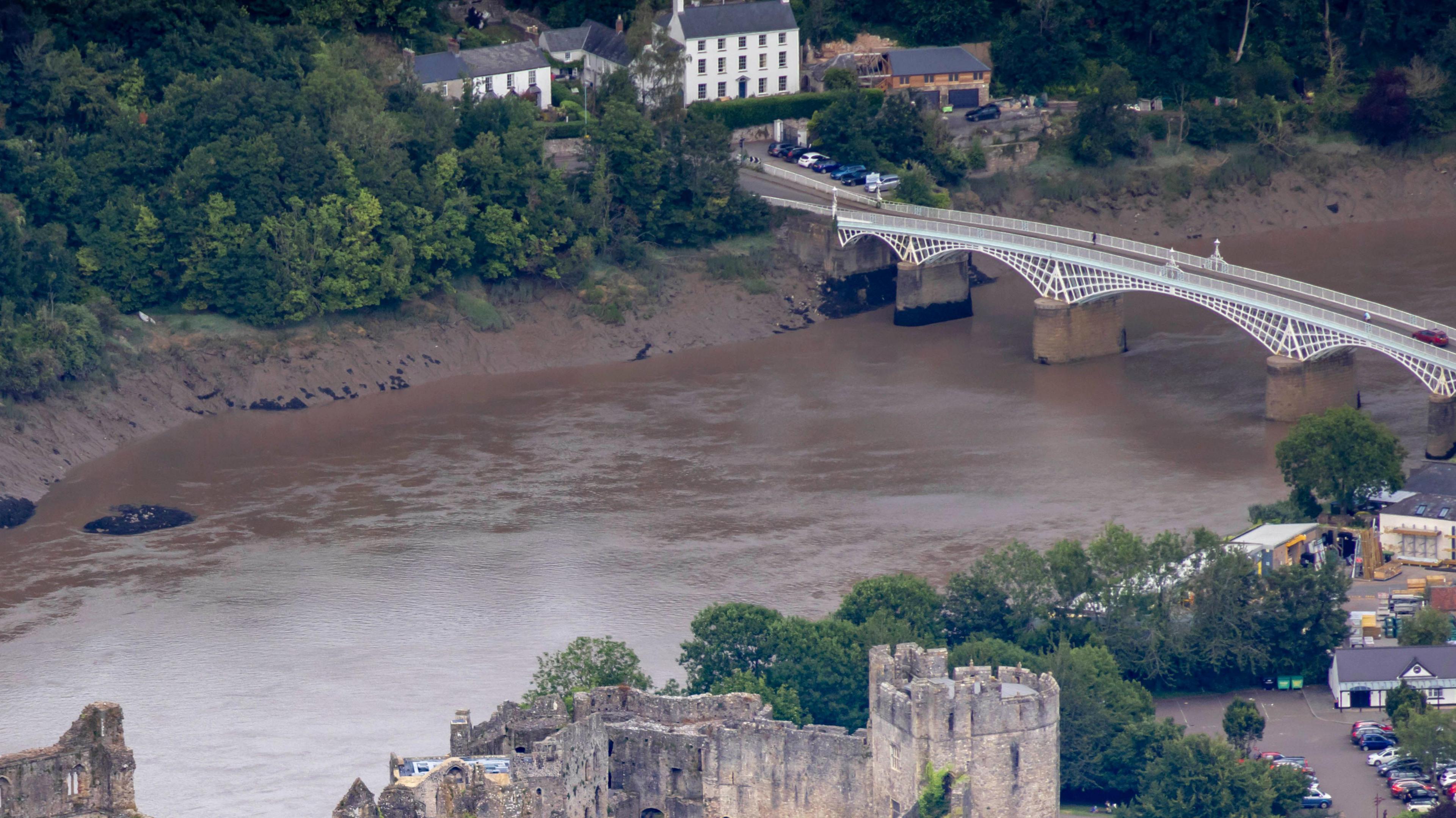 The brown water and muddy banks of the River Wye, pictured flowing between the town of Chepstow, Monmouthshire, and the village of Tutshill, Gloucestershire