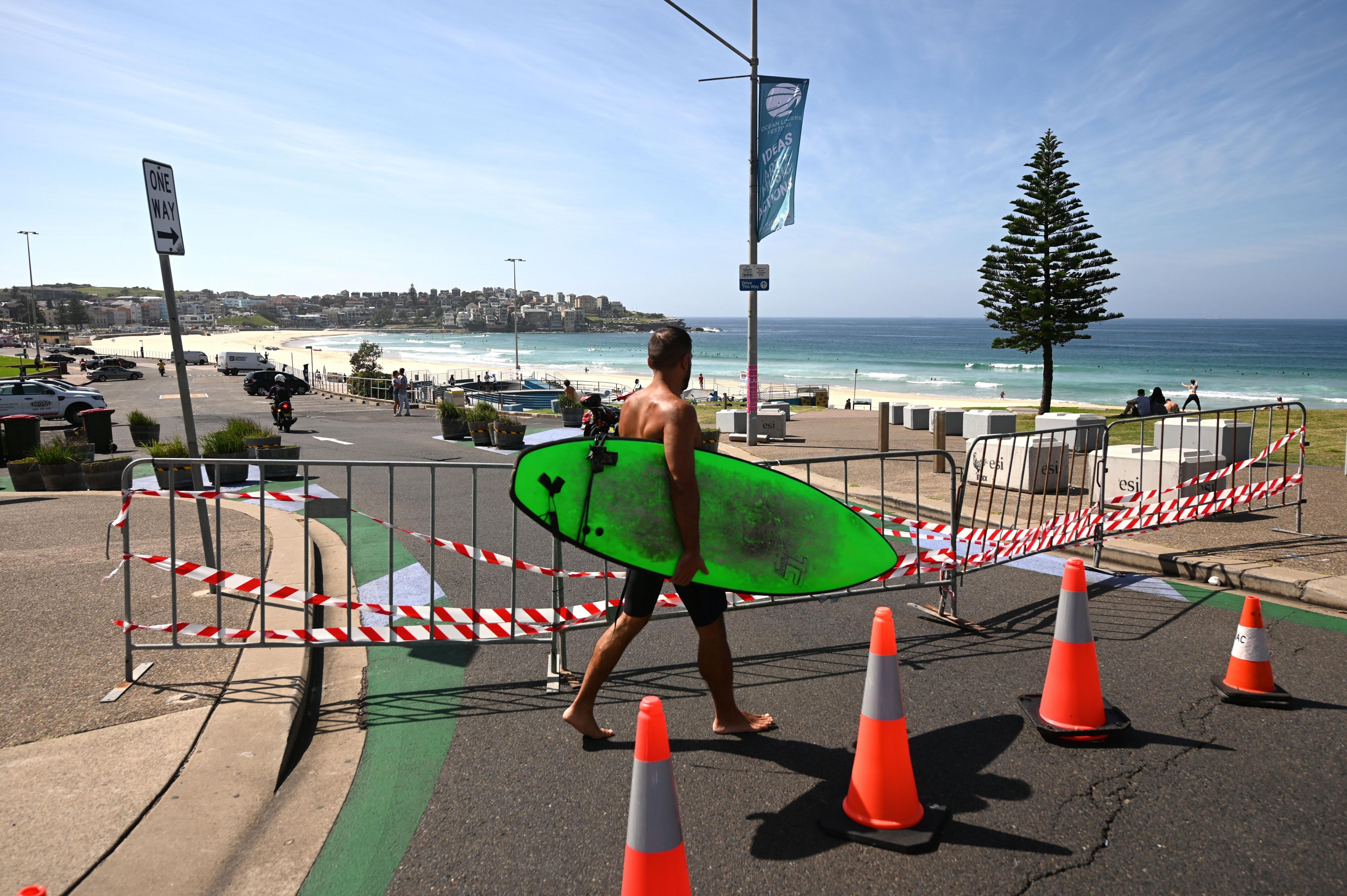 A surfer walks in front of a fence near Bondi Beach