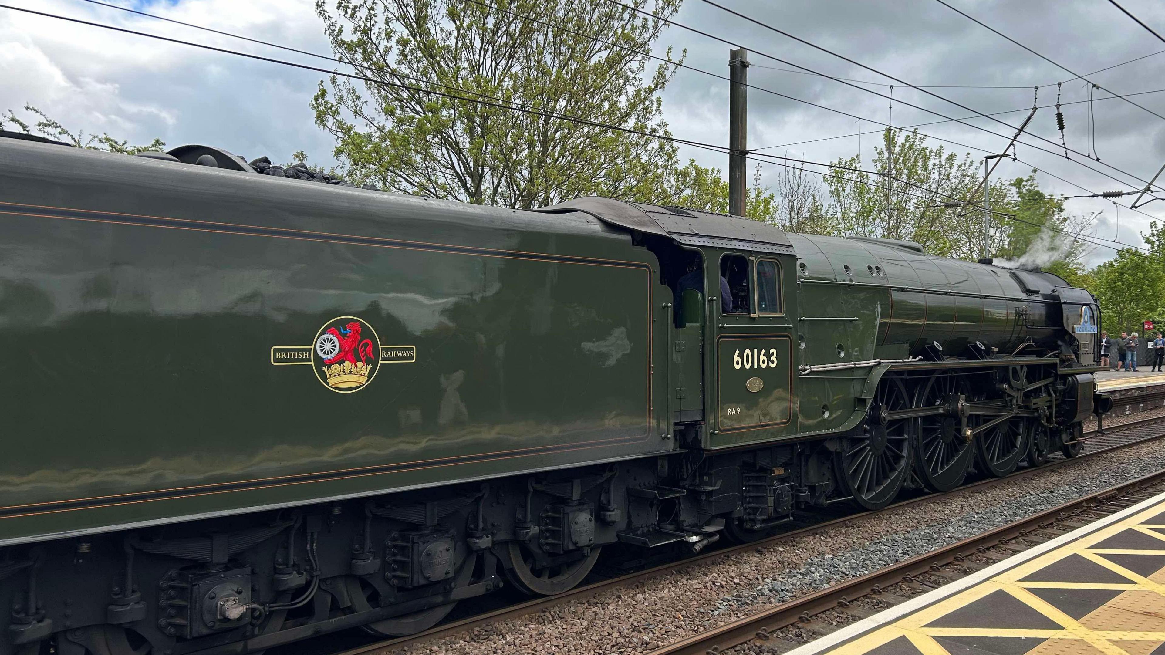 A green steam train pulls into a station.