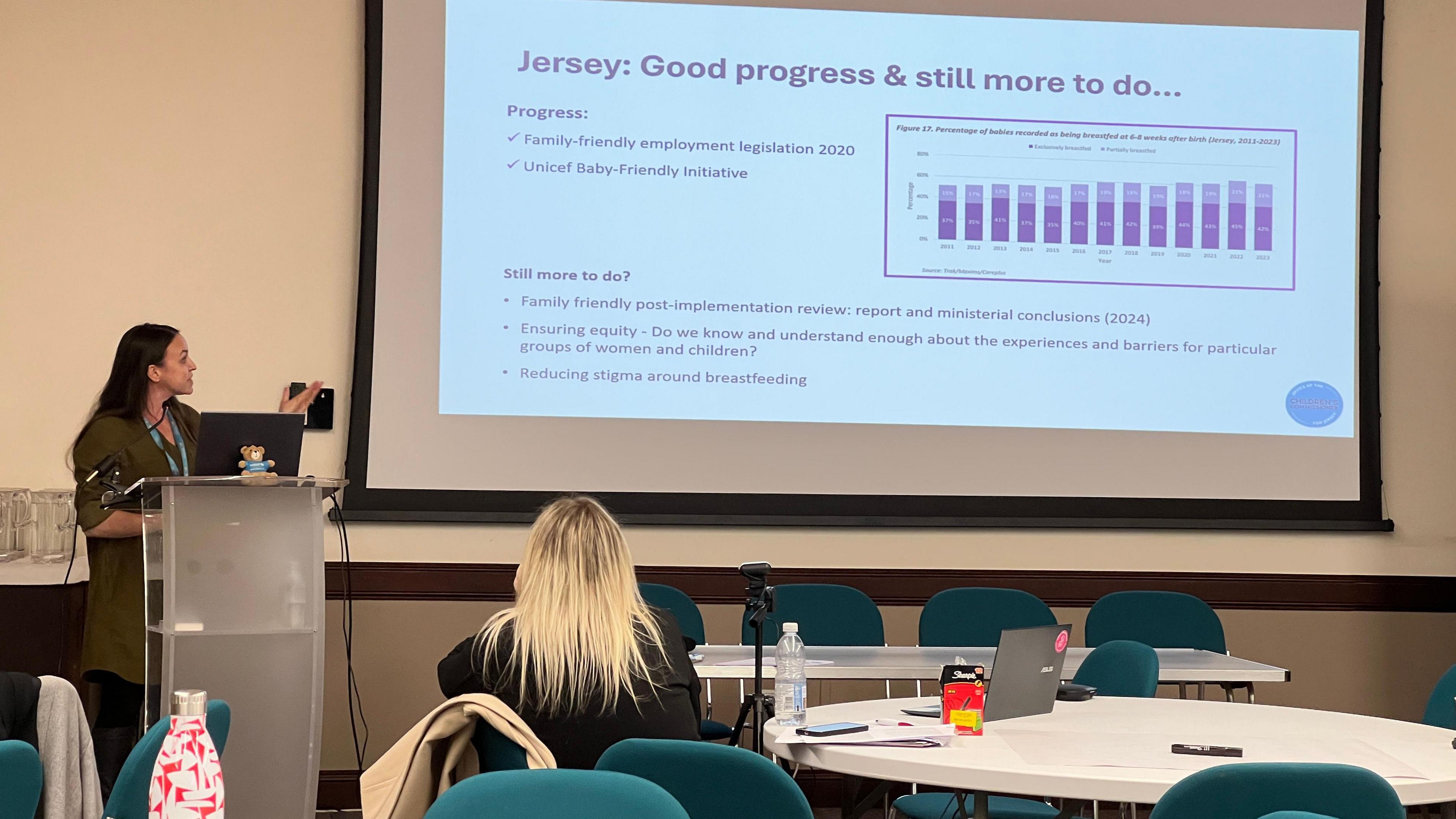 A woman in front of a stand as she gestures to a projector screen which has statistics on Jersey employment legislation.