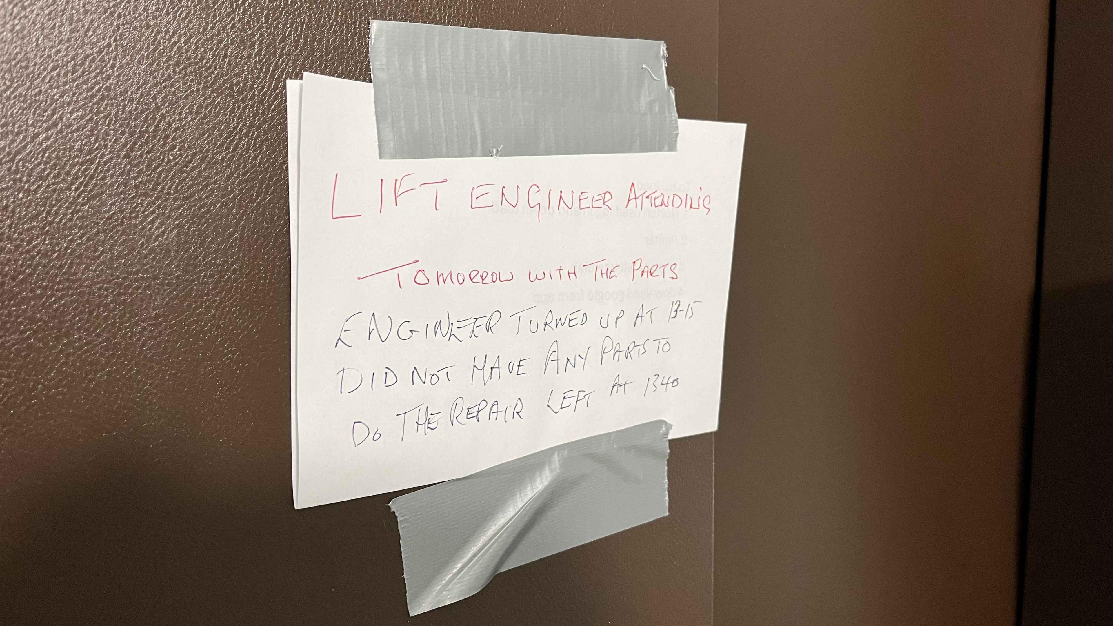 A handwritten sign stuck to the brown lift door with duct tape saying the engineer didnt have parts to repair the lift