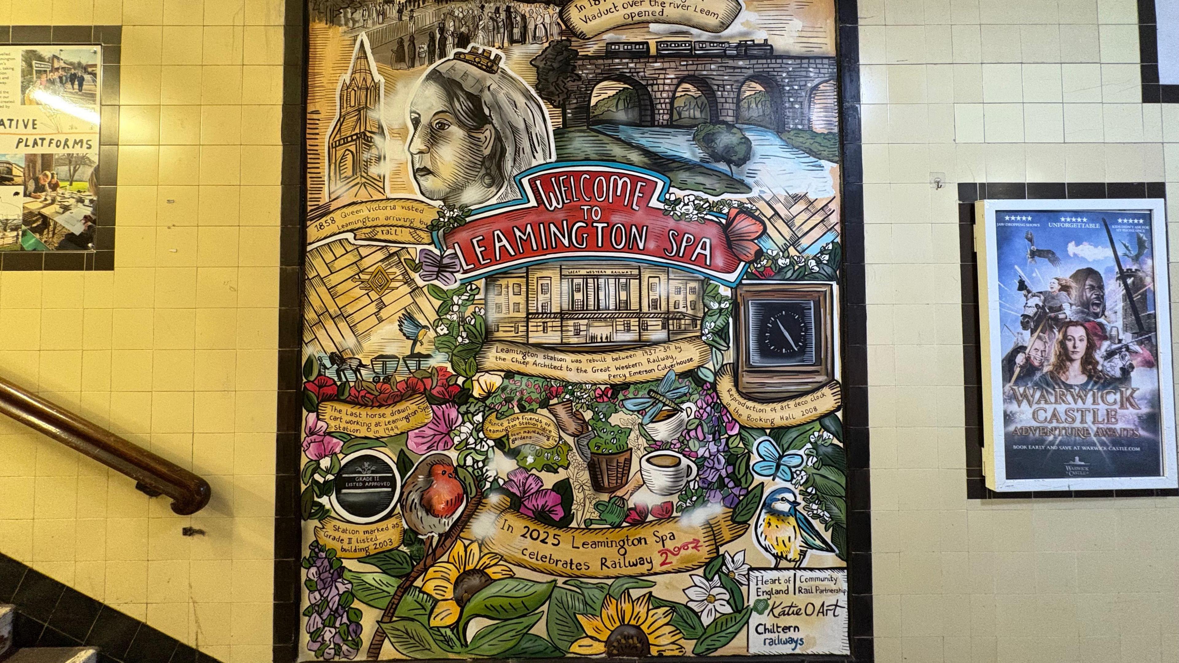 A colourful mural on the side of a wall at a train station. The mural reads 'Welcome to Leamington Spa'. Other posters and a bannister can be seen in the background.