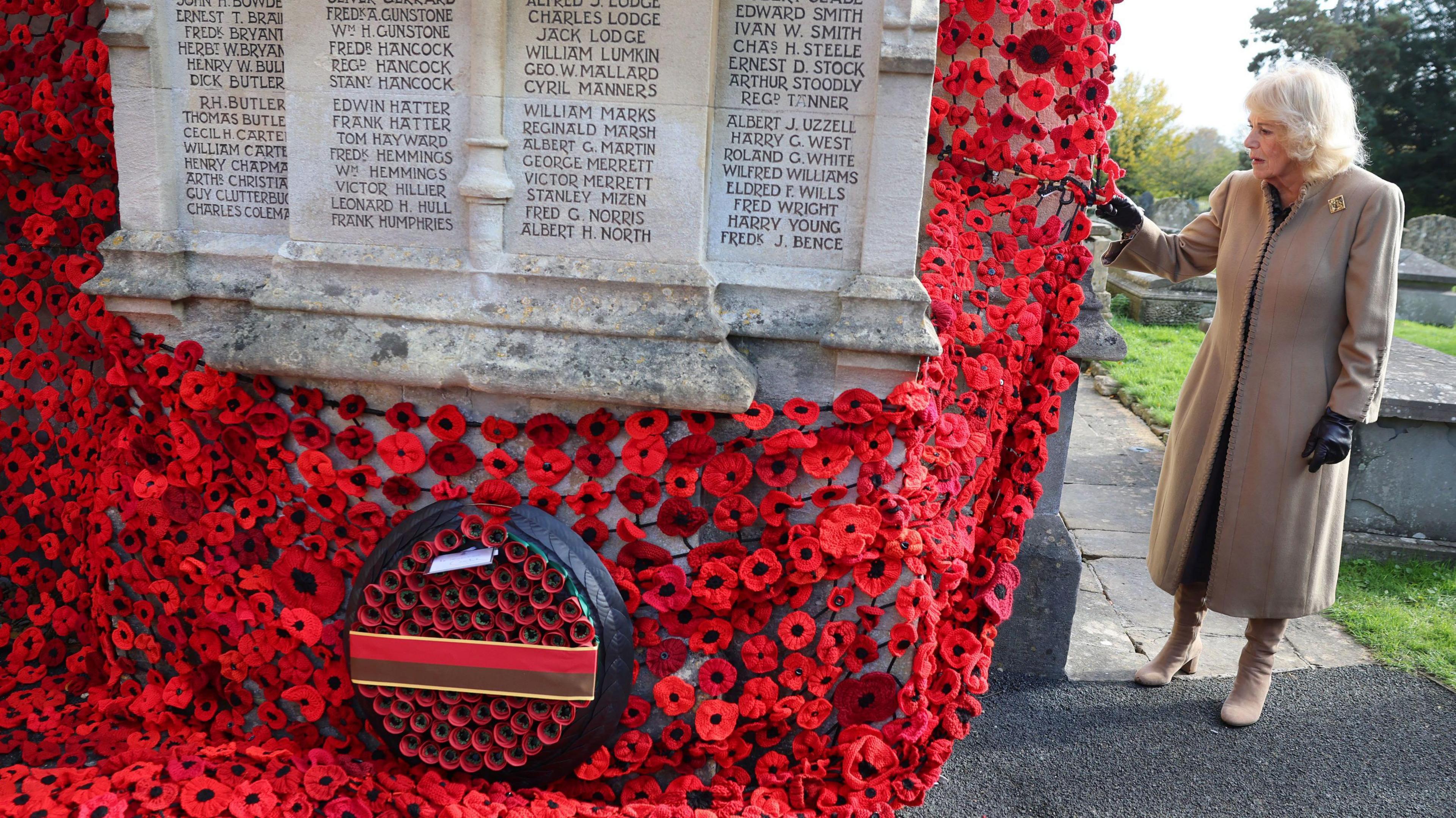 Camilla places a poppy on a wider display of poppies attached to a white war memorial