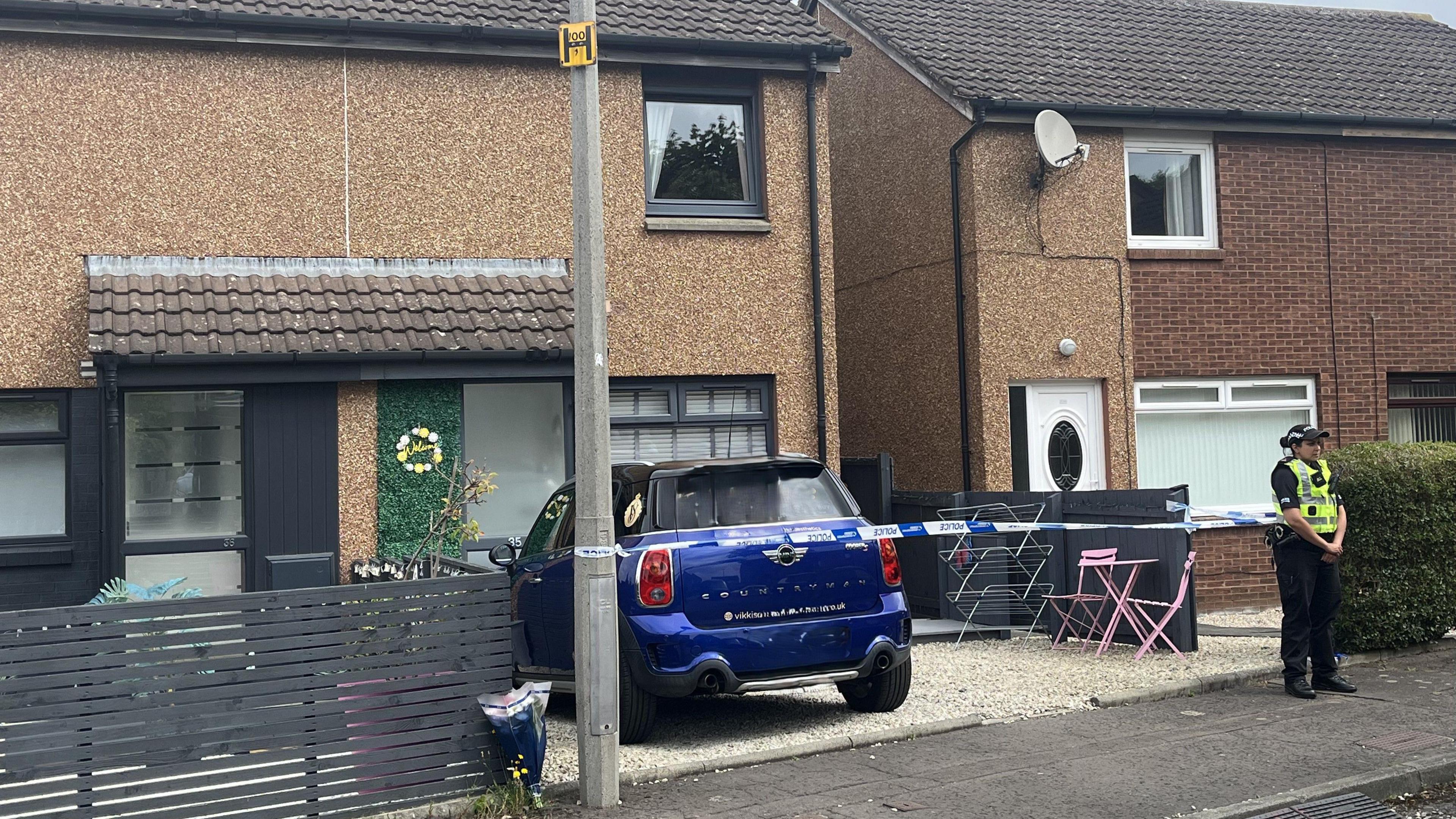 A female police officer stands outside a cordoned-off house.