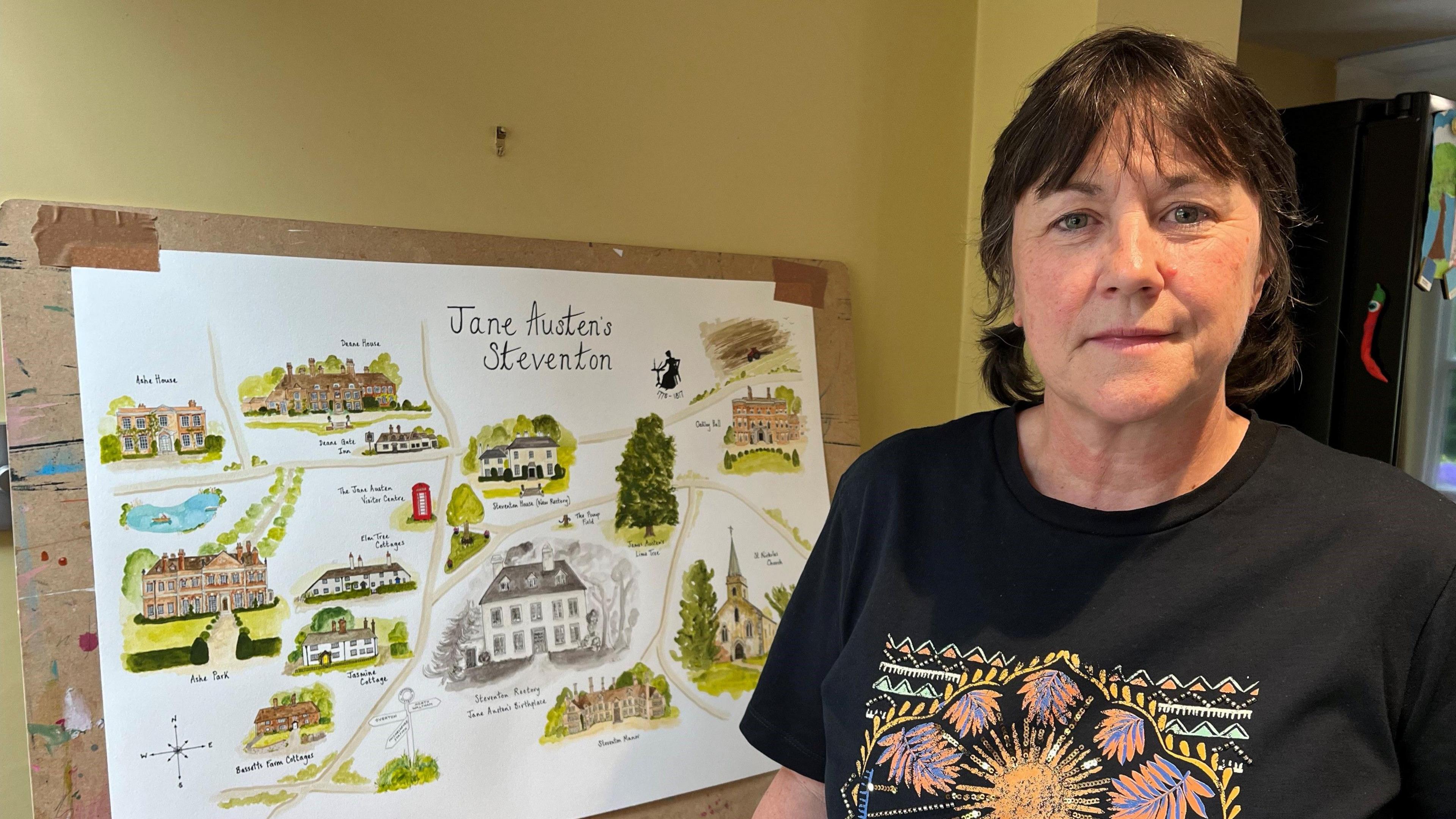 A woman stands in front of a picture entitled Jane Austen's Steventon which has illustrations of old buildings in the area that are connected to the writer